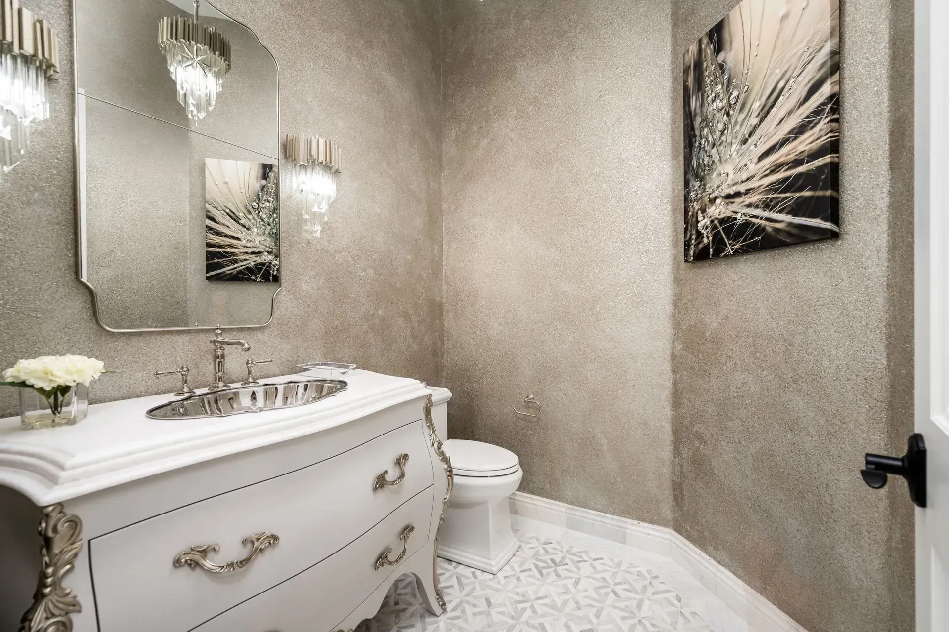 Luxurious powder room with a white ornate vanity, shimmering walls, and art.