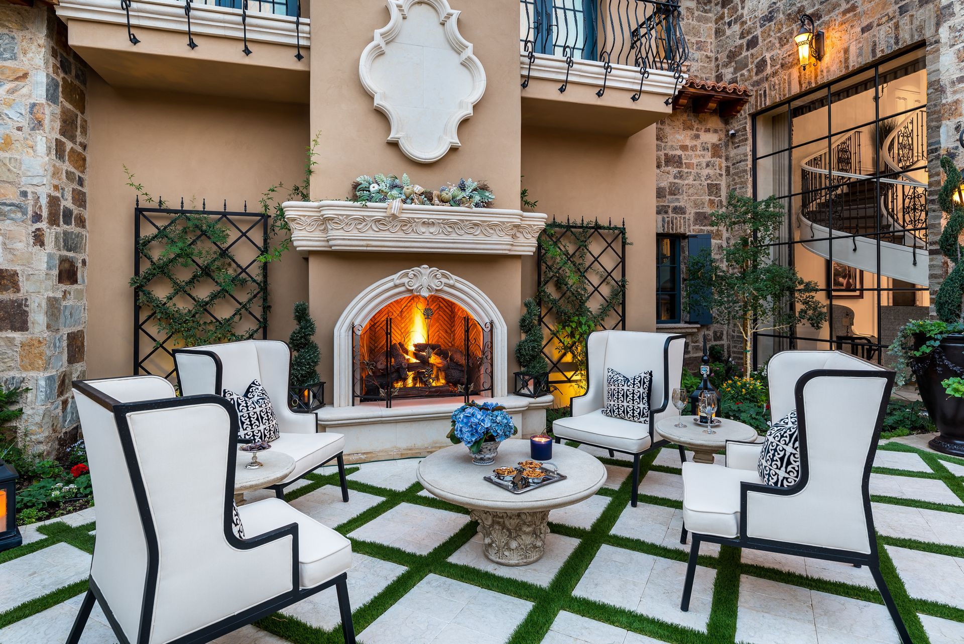 Elegant outdoor patio with white chairs around a fire pit and lit stone fireplace at dusk