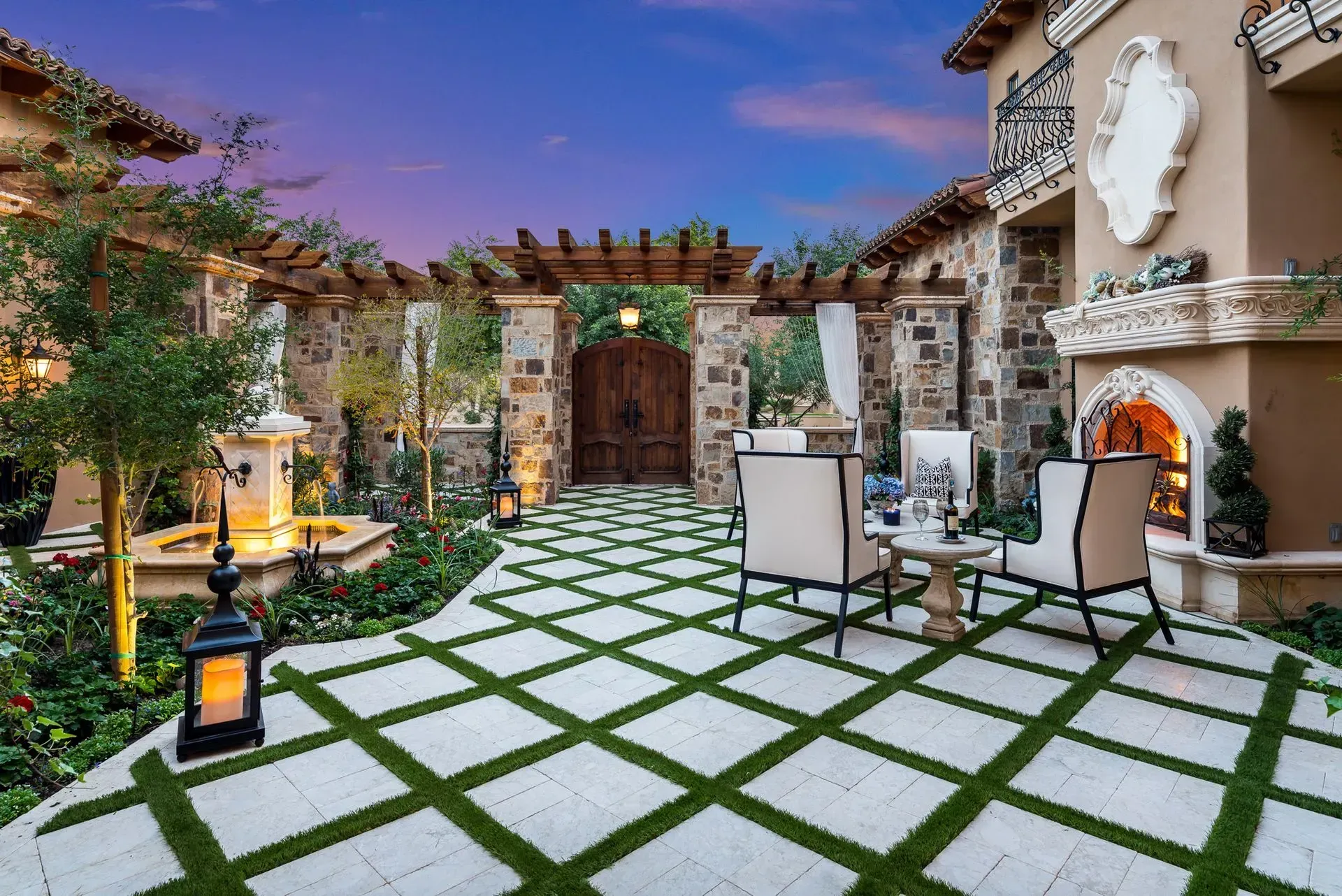 Patio with patterned stone and grass, fountain, wooden pergola, and two chairs.