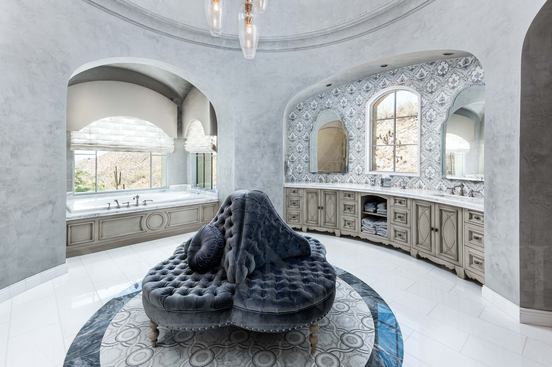 Luxury master bathroom with ornate cabinetry, arched windows, mosaic backslash, and a dark sculptural sofa in the center of the room.