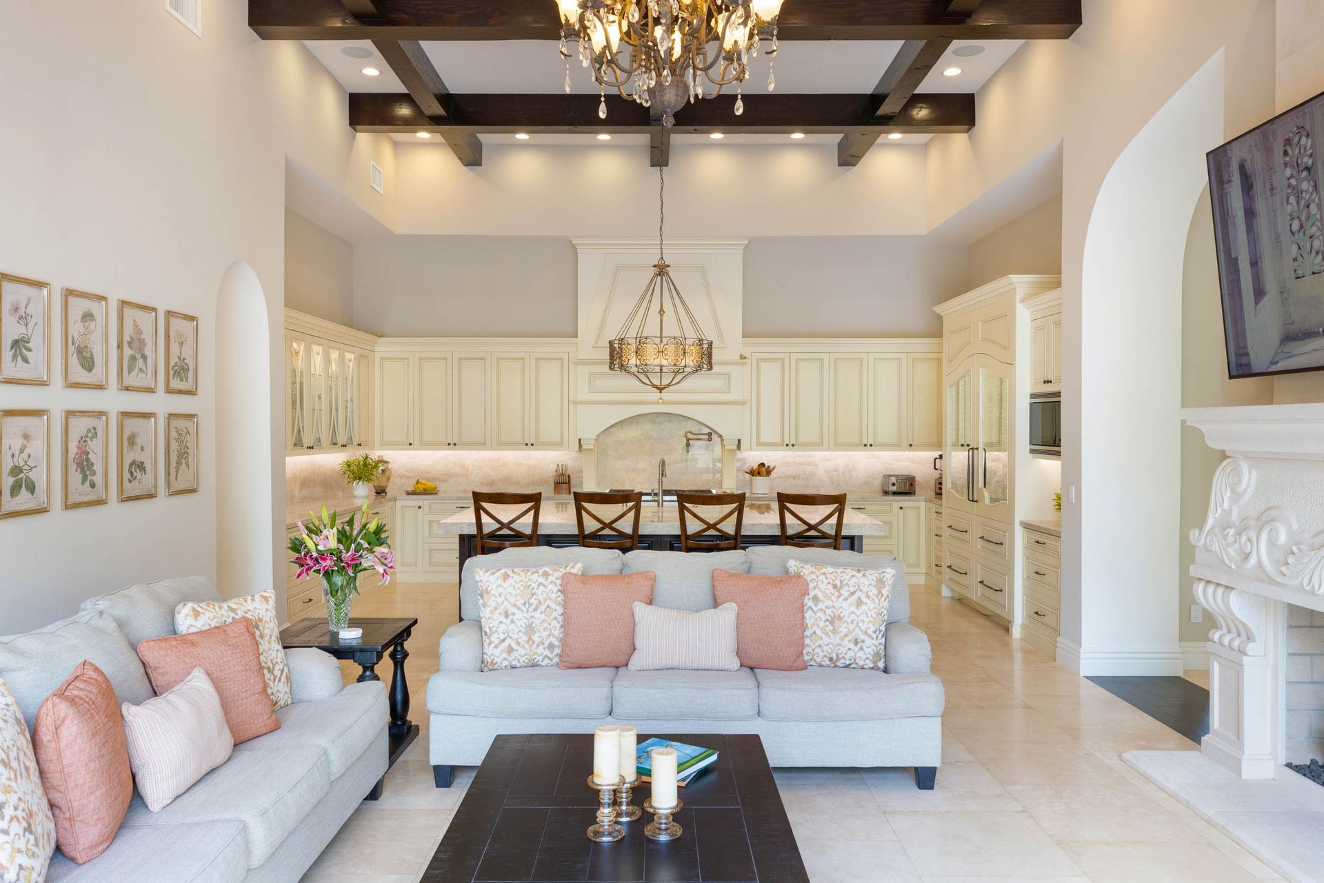 Living room with open kitchen. Gray sofa, pink pillows, dark wood coffee table, beige cabinetry, chandelier.