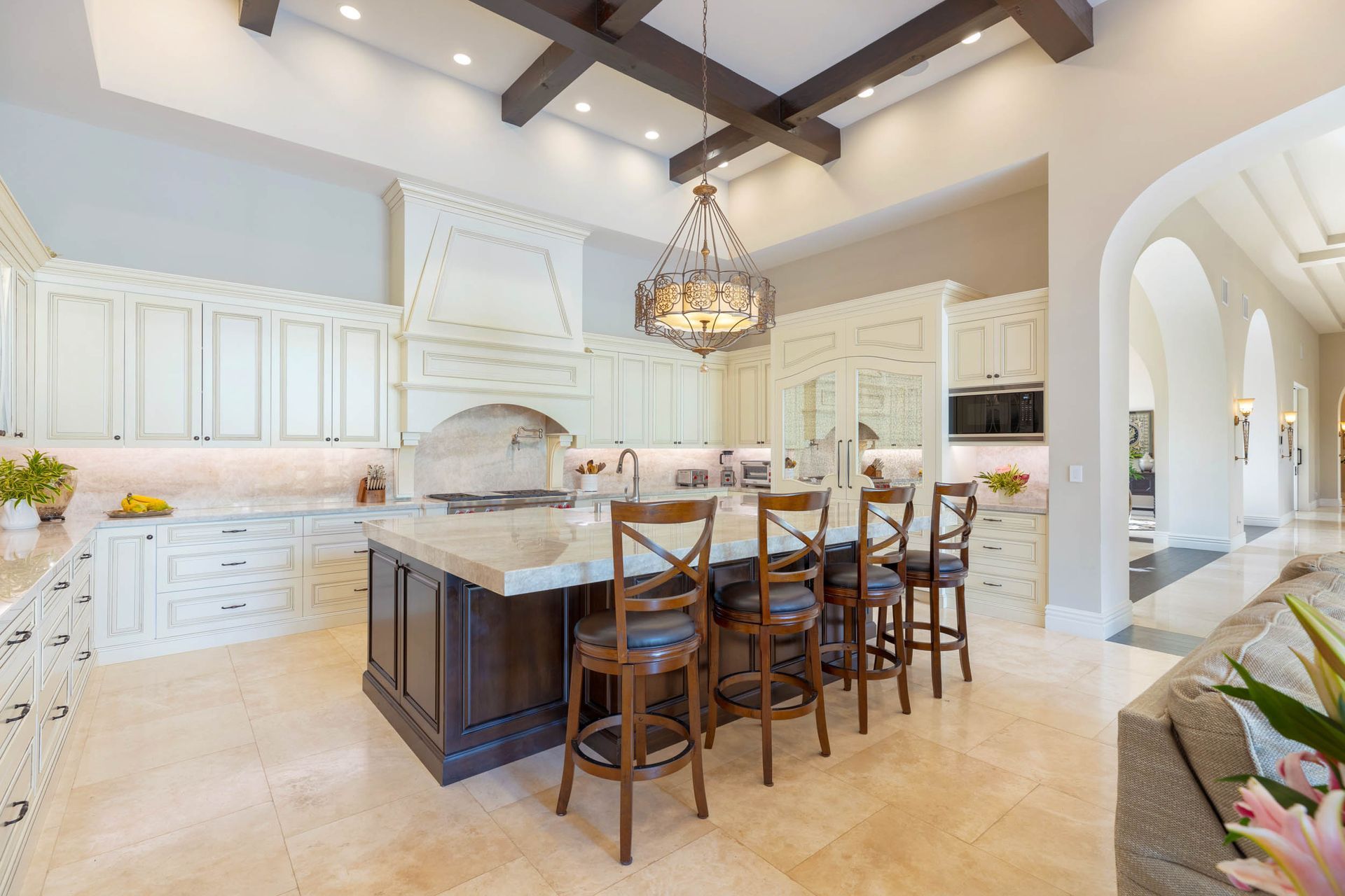 Spacious kitchen with a large island, wooden beams, and white cabinets. Bar stools at the island.