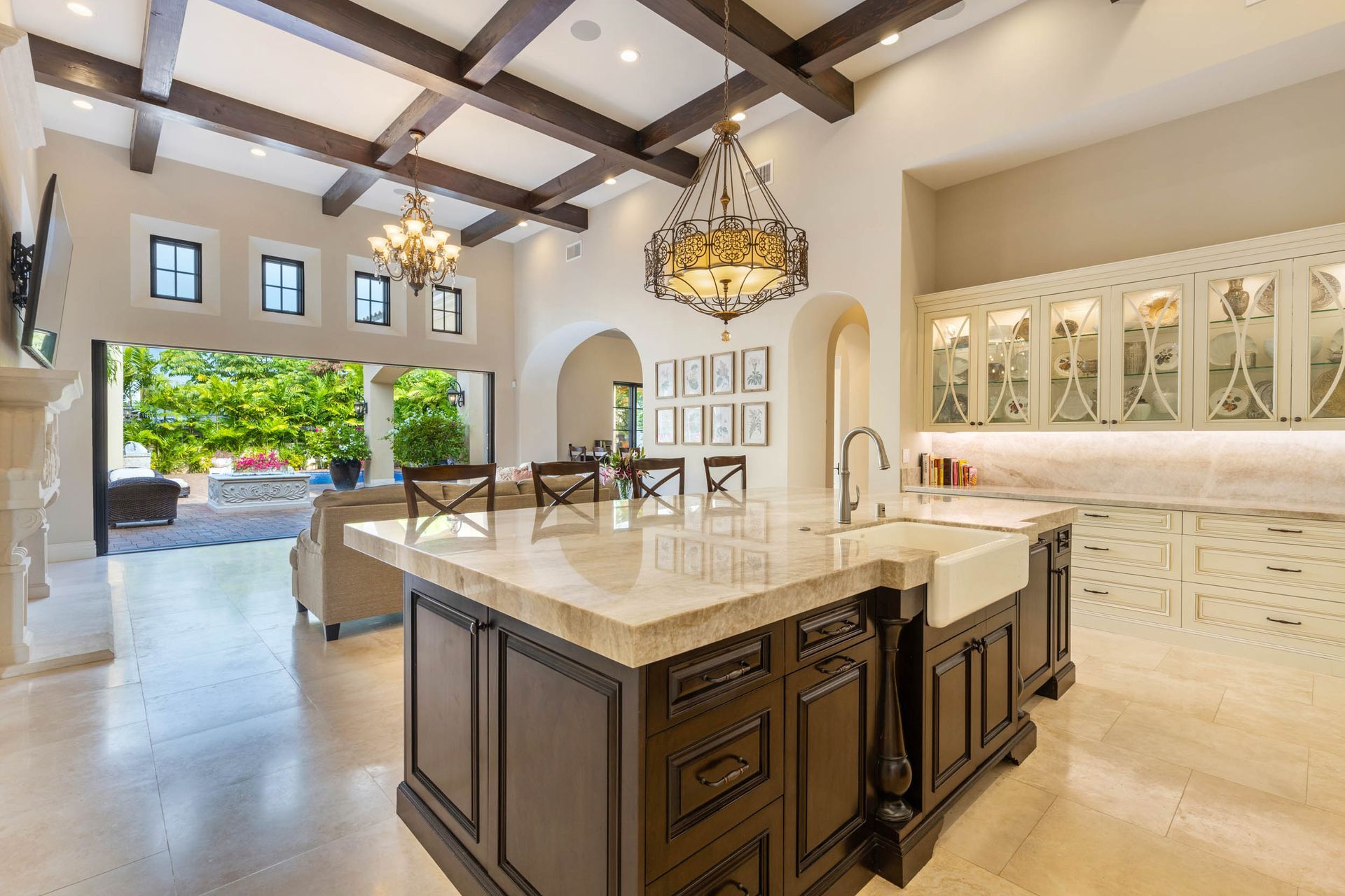Open-plan kitchen with dark wood island, ornate chandelier, and view of patio.
