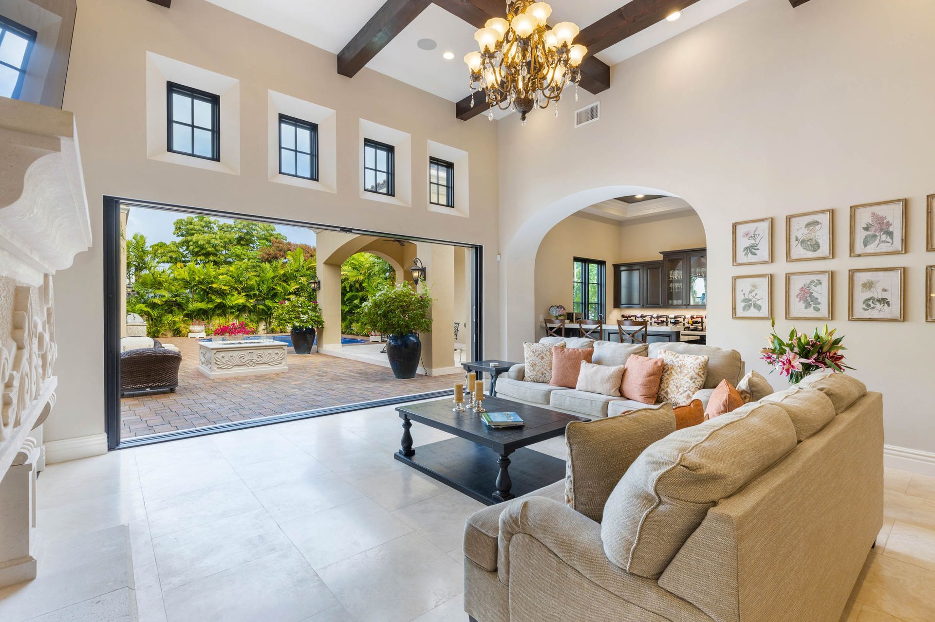 Living room with open doors to a patio. Beige couches, black coffee table, stone floor.