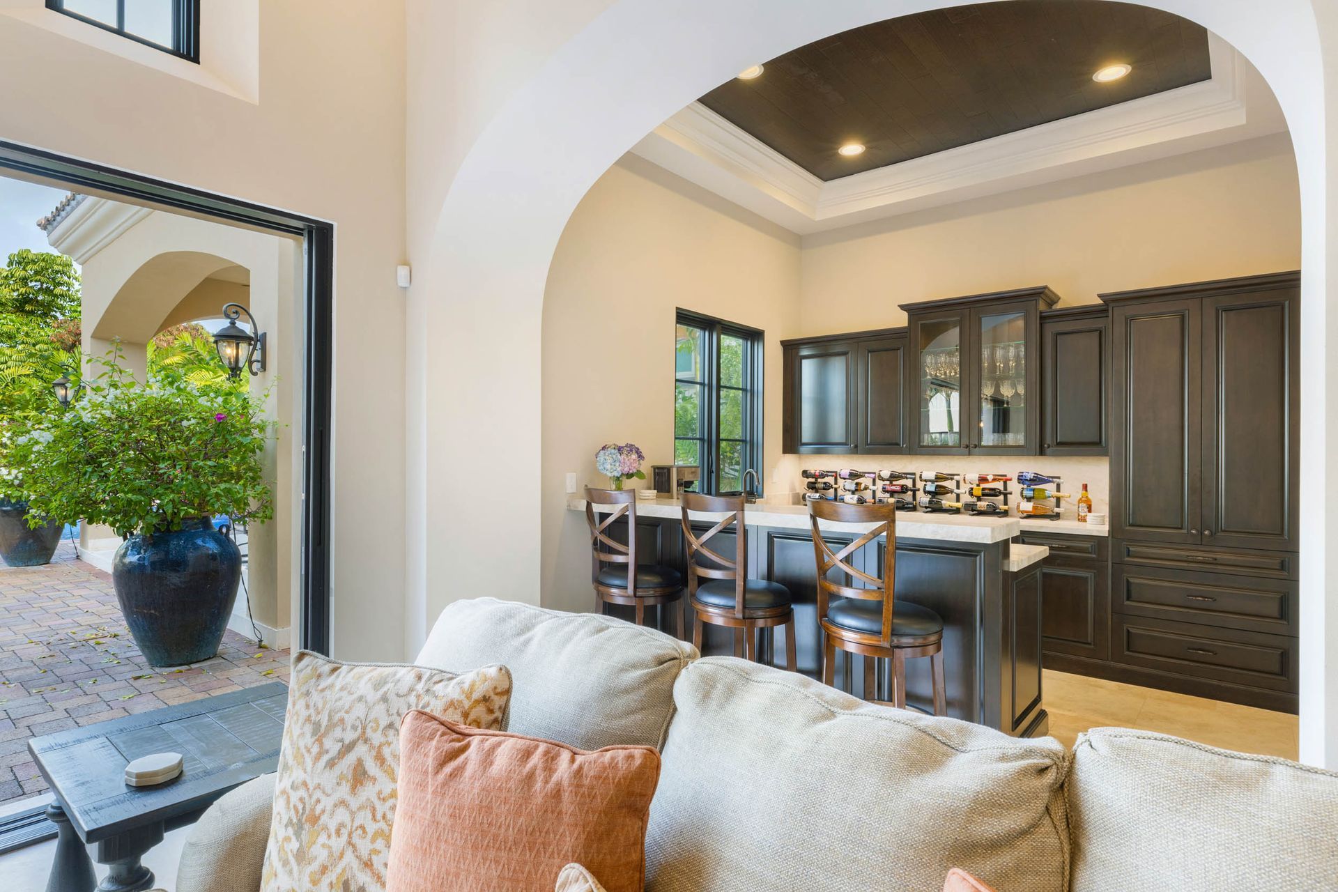 Living room with a bar area. Sliding door to patio with large potted plant. Beige walls, dark cabinets.