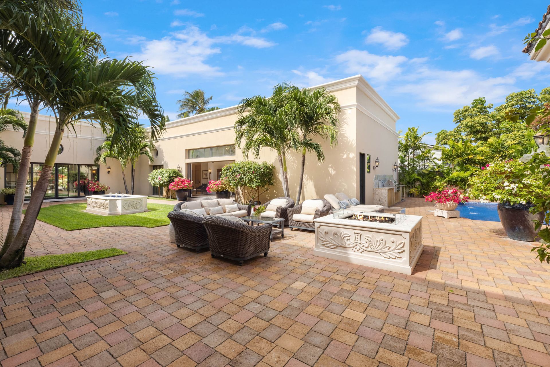 Patio with seating, fire pit, and lush landscaping on a sunny day.