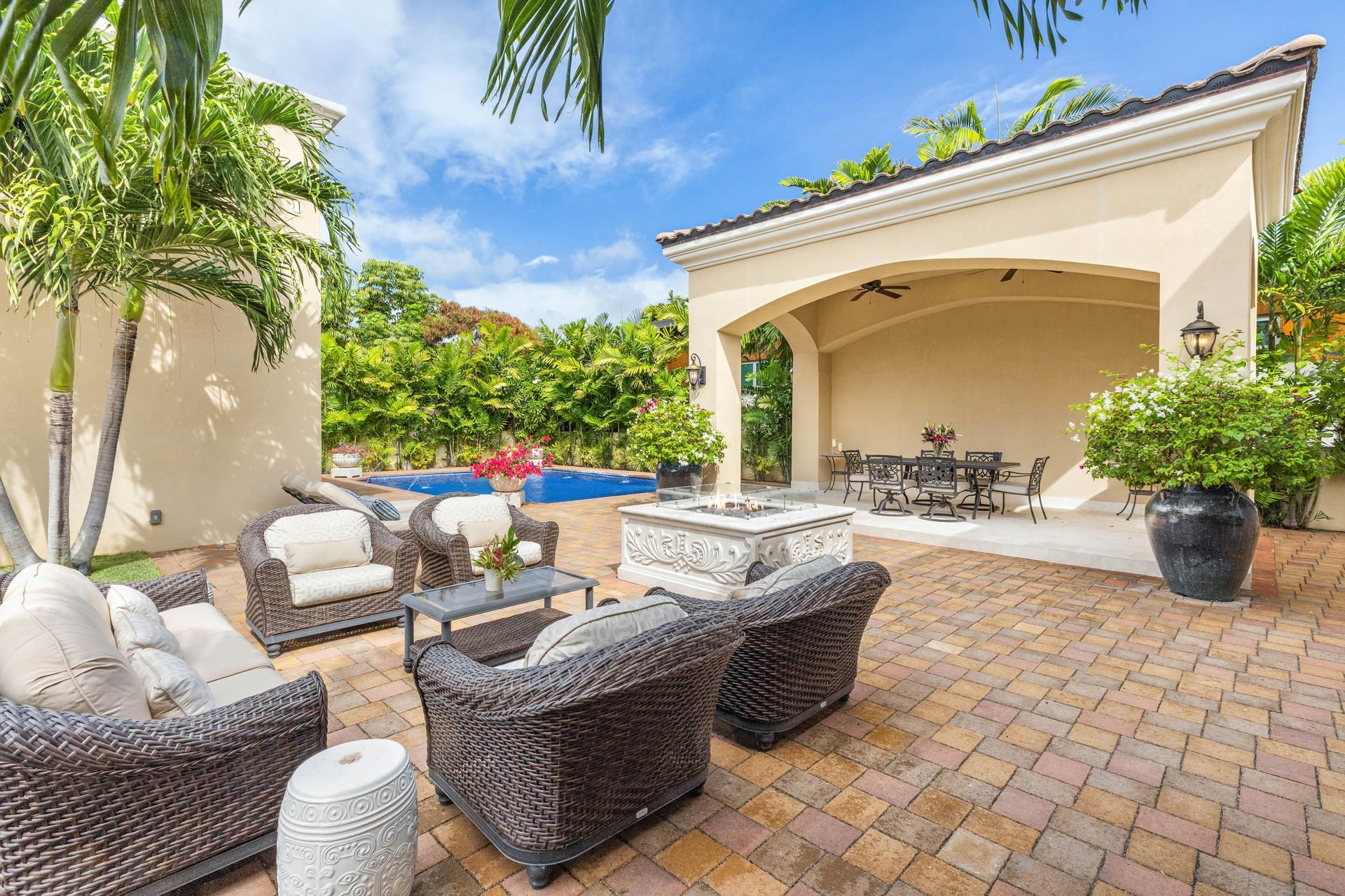 Patio with seating, fireplace, and arched dining area, near a pool, under a bright sky.