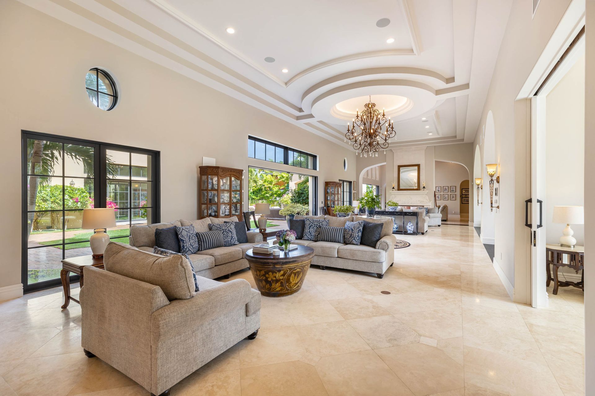 Spacious living room with marble floors, a large sofa, and a chandelier; doors lead to outdoor space.