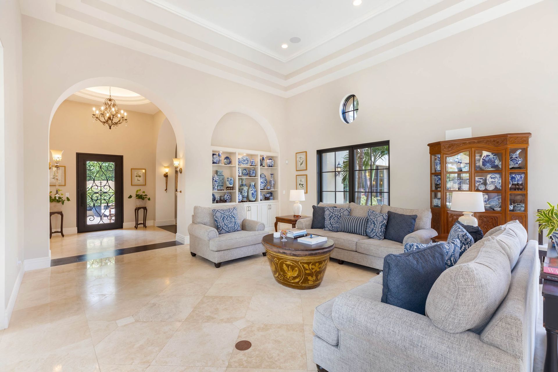 Spacious living room with neutral tones, arched doorways, multiple sofas, and a display cabinet.