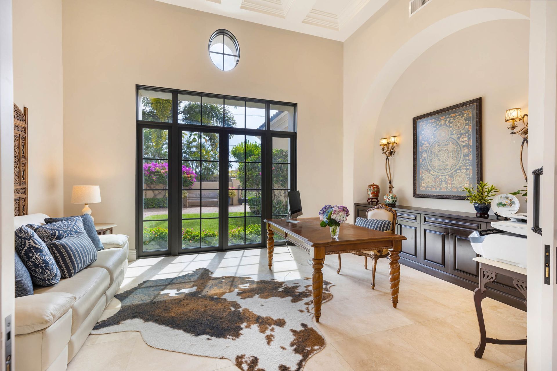 Elegant home office with a large wooden desk, cowhide rug, and French doors leading to a garden.