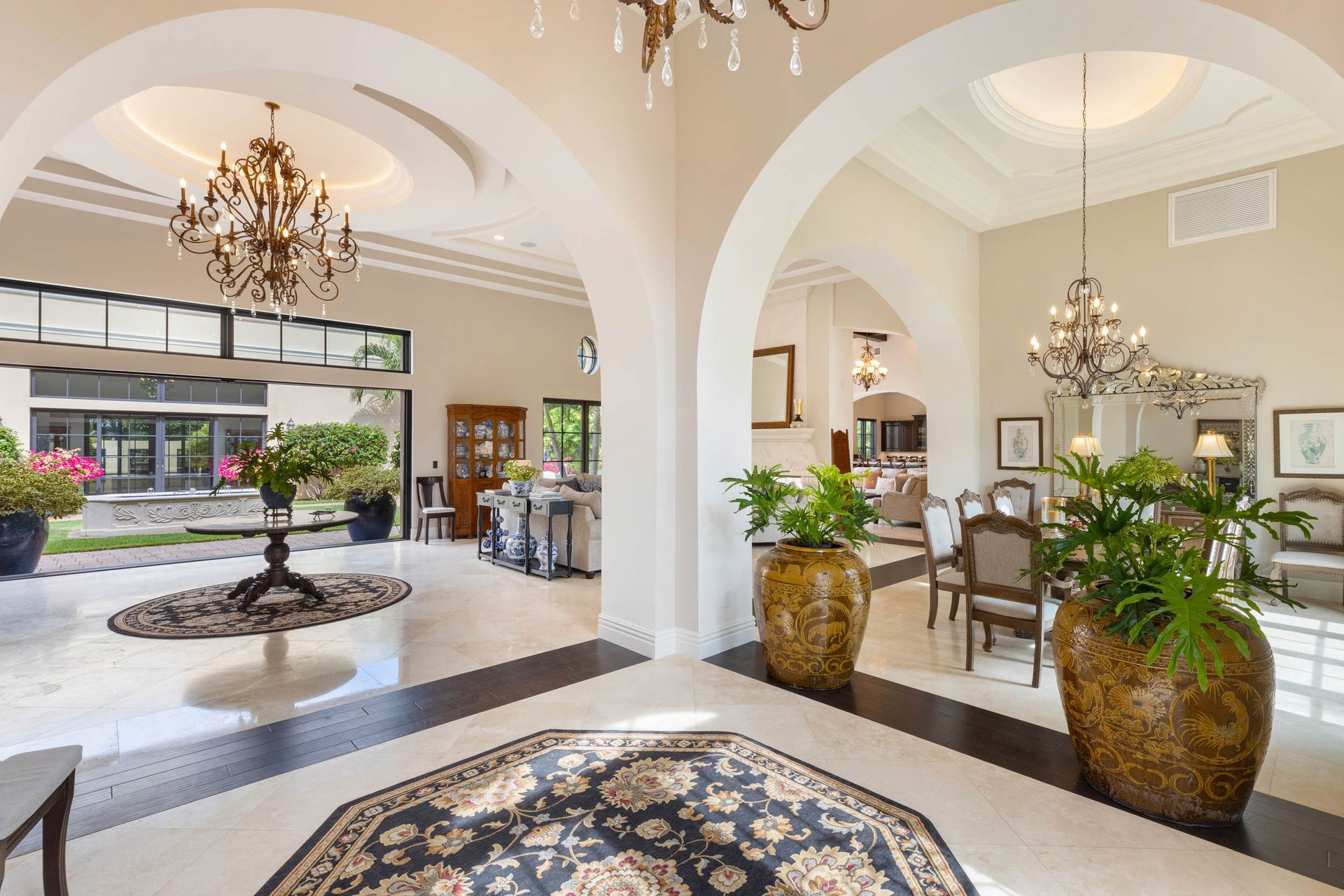 Elegant lobby with archways, chandeliers, potted plants, and patterned floor.