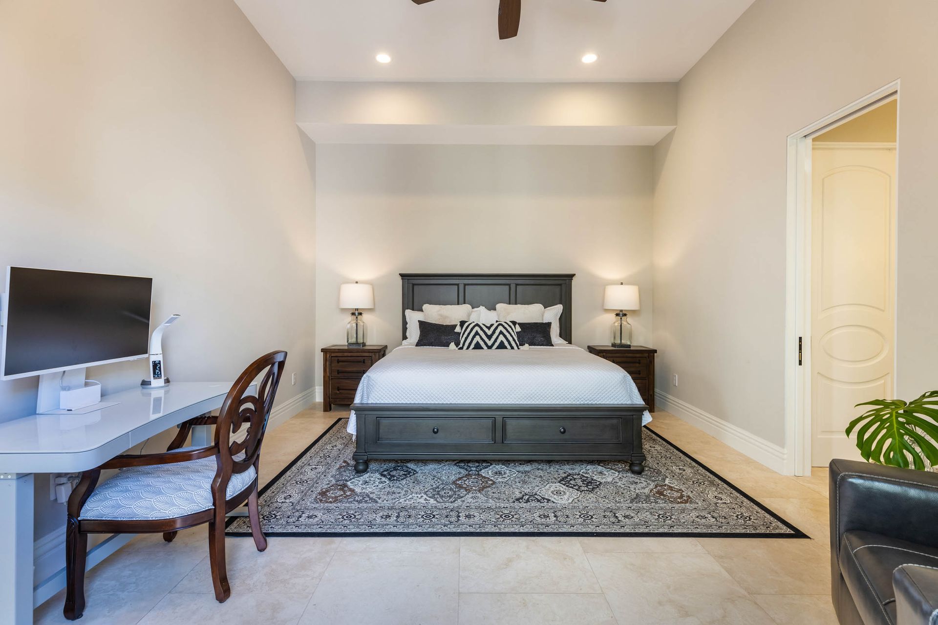 Bedroom with desk, bed, rug, and side tables. Neutral walls, dark furniture, and natural light.