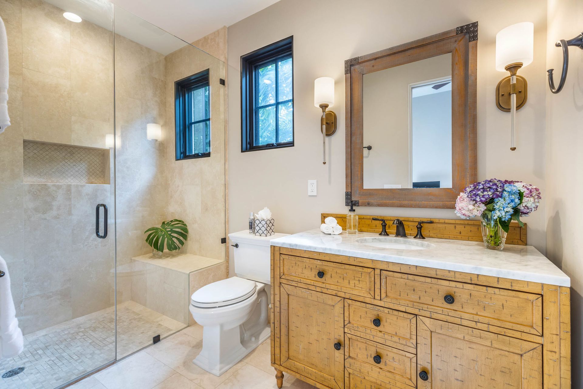 Bathroom with a glass shower, wooden vanity, and large mirror. Neutral walls and natural light.
