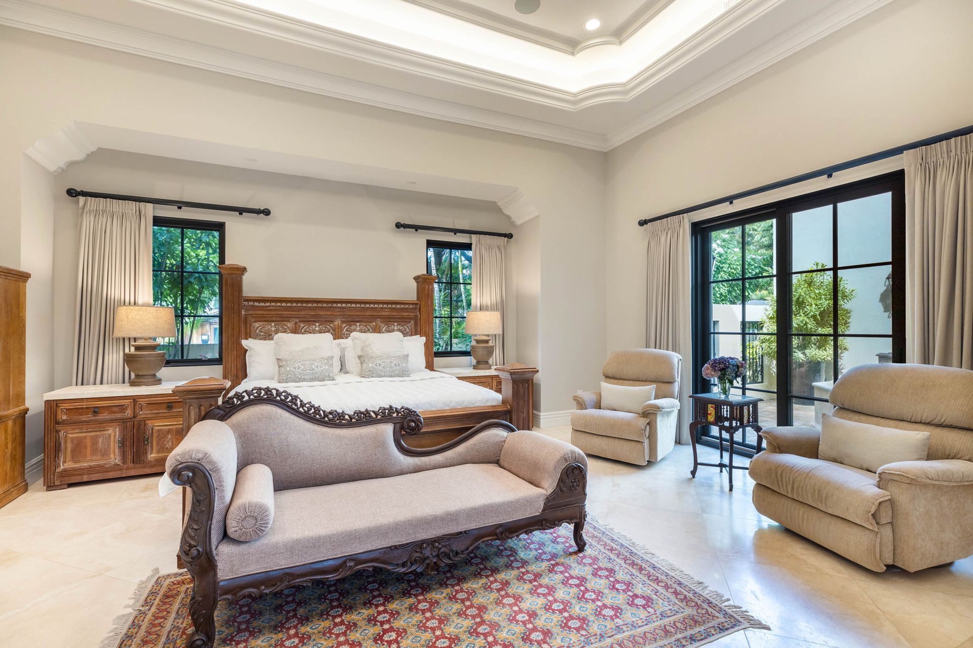 Spacious bedroom with ornate bed, chaise lounge, two armchairs, and patio access.
