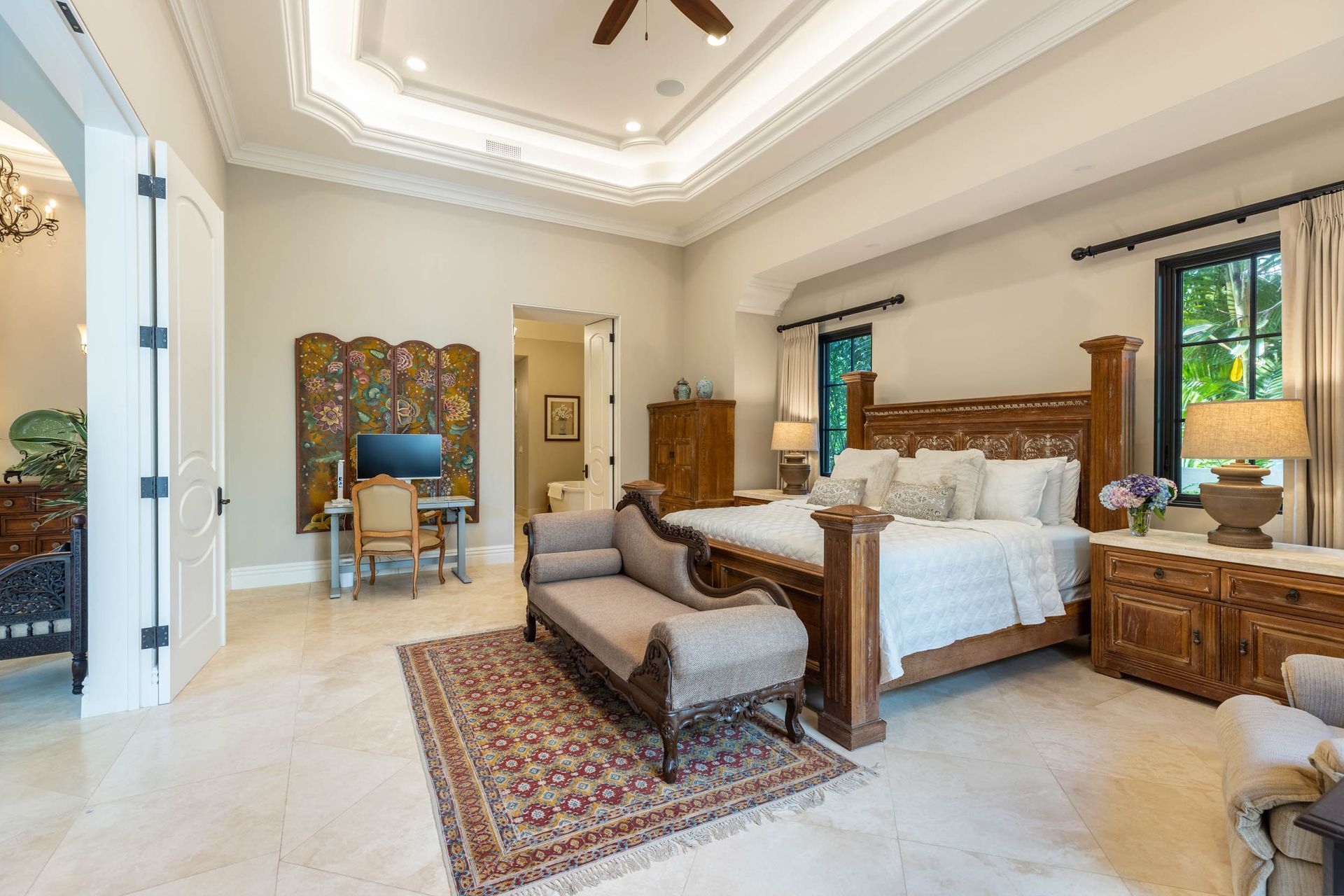Spacious bedroom with ornate wooden bed, desk area, seating, and decorative ceiling details.