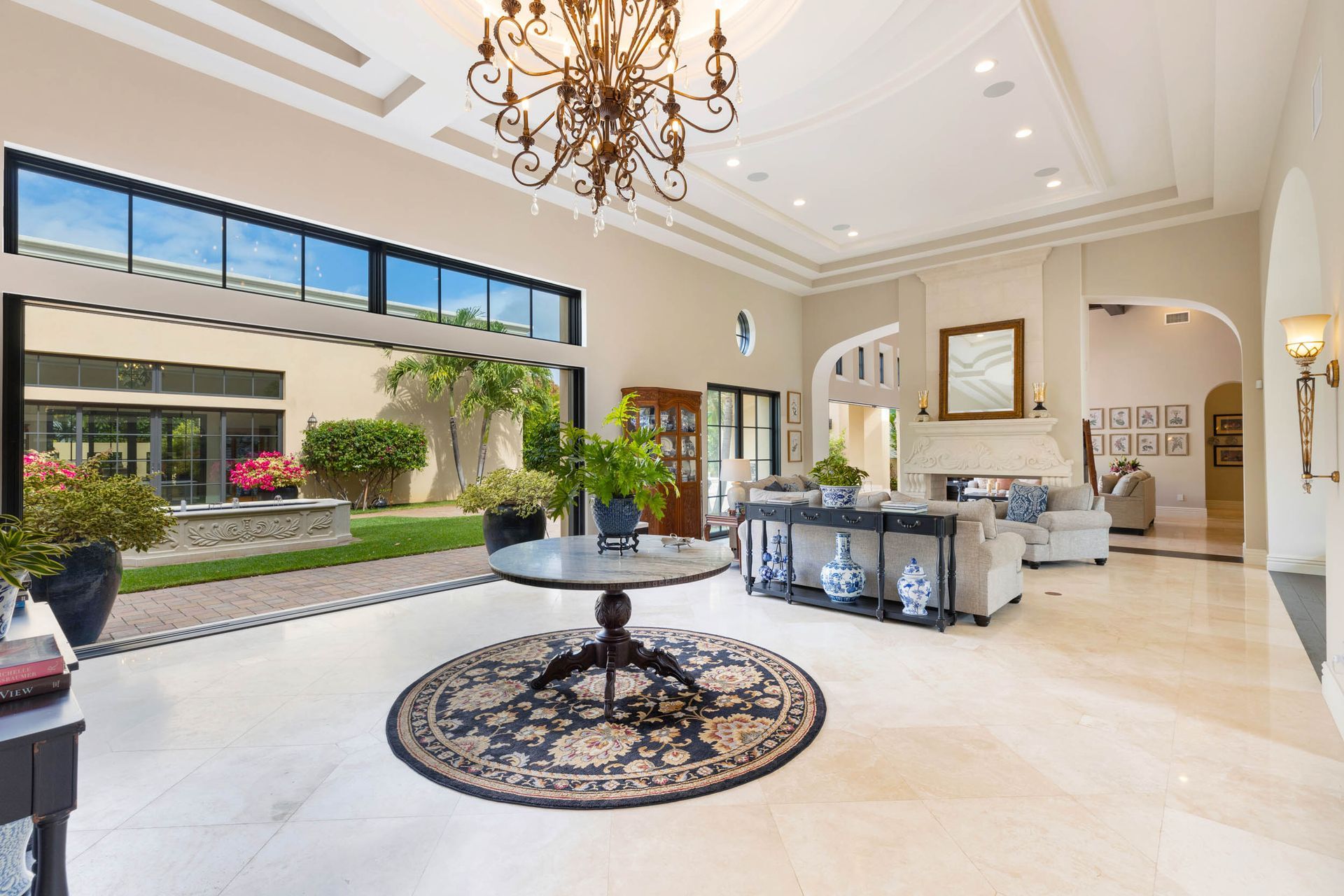 Spacious foyer with marble floor, chandelier, large windows, and a round table on a rug.