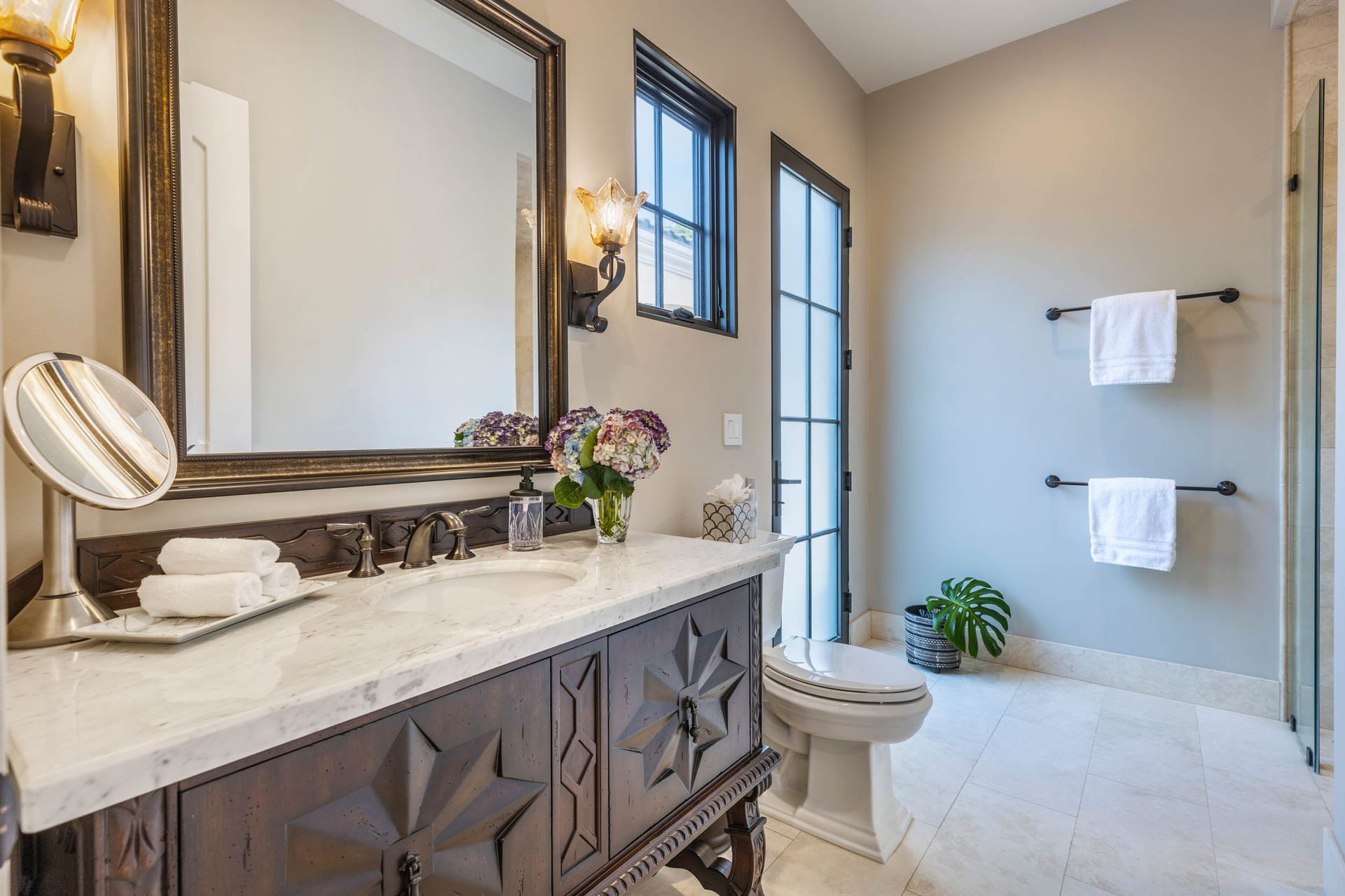 Bathroom with vanity, toilet, and towels on a wall-mounted rack. Beige and dark brown colors.