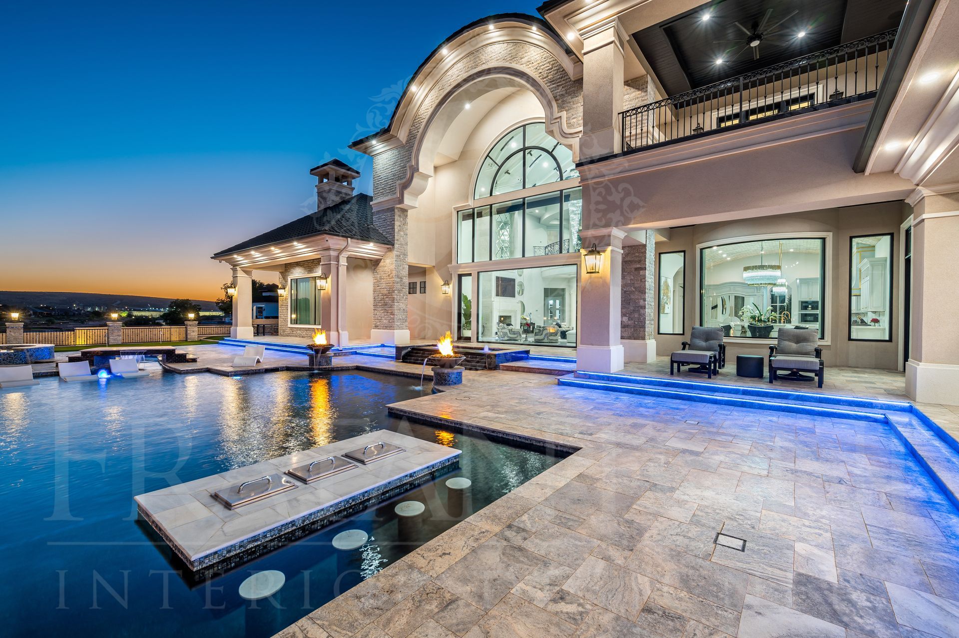 Luxury mansion with pool, patio, and outdoor fireplace at dusk; blue and white color scheme. Pool has an in-pool bar with seating designed by Fratantoni Interior Designers in scottsdale, arizona
