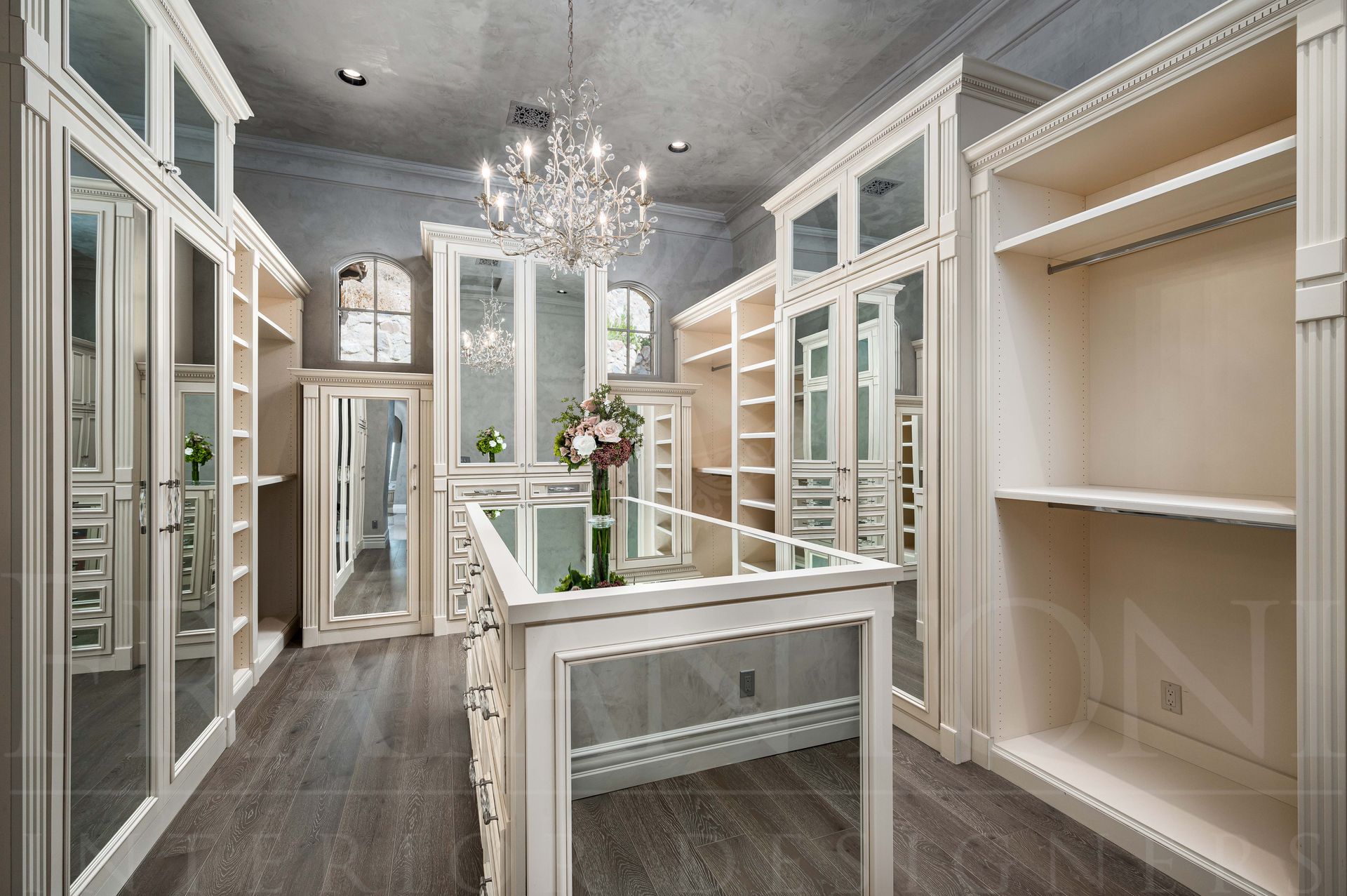 Elegant walk-in closet with white built-in shelving, mirrored doors, wood floors, and a chandelier in DC Ranch Arizona