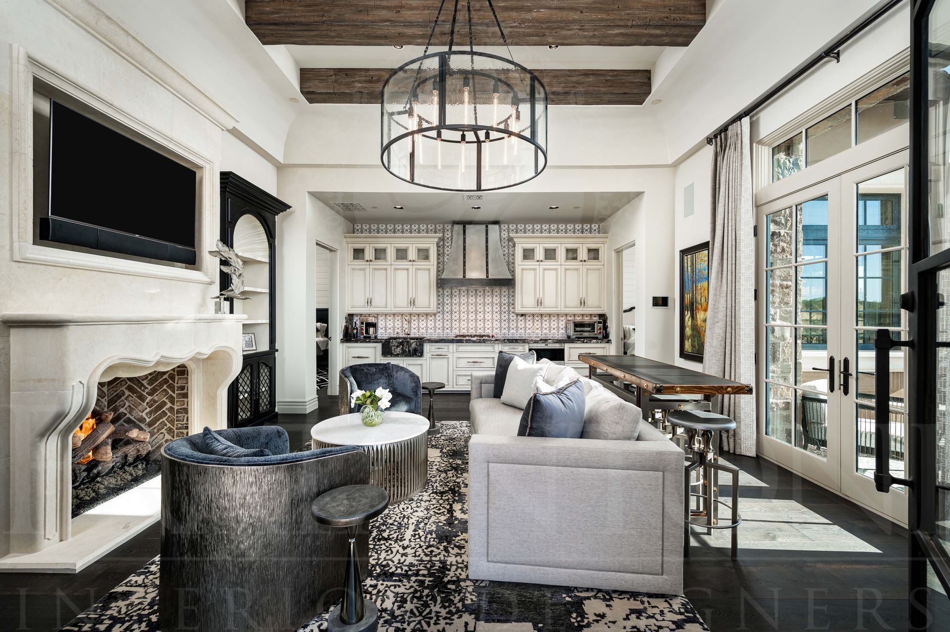 Bright elegant casita living room with stone fireplace, chandelier, kitchen view, and large glass doors to outdoors designed by Fratantoni Interior Designers