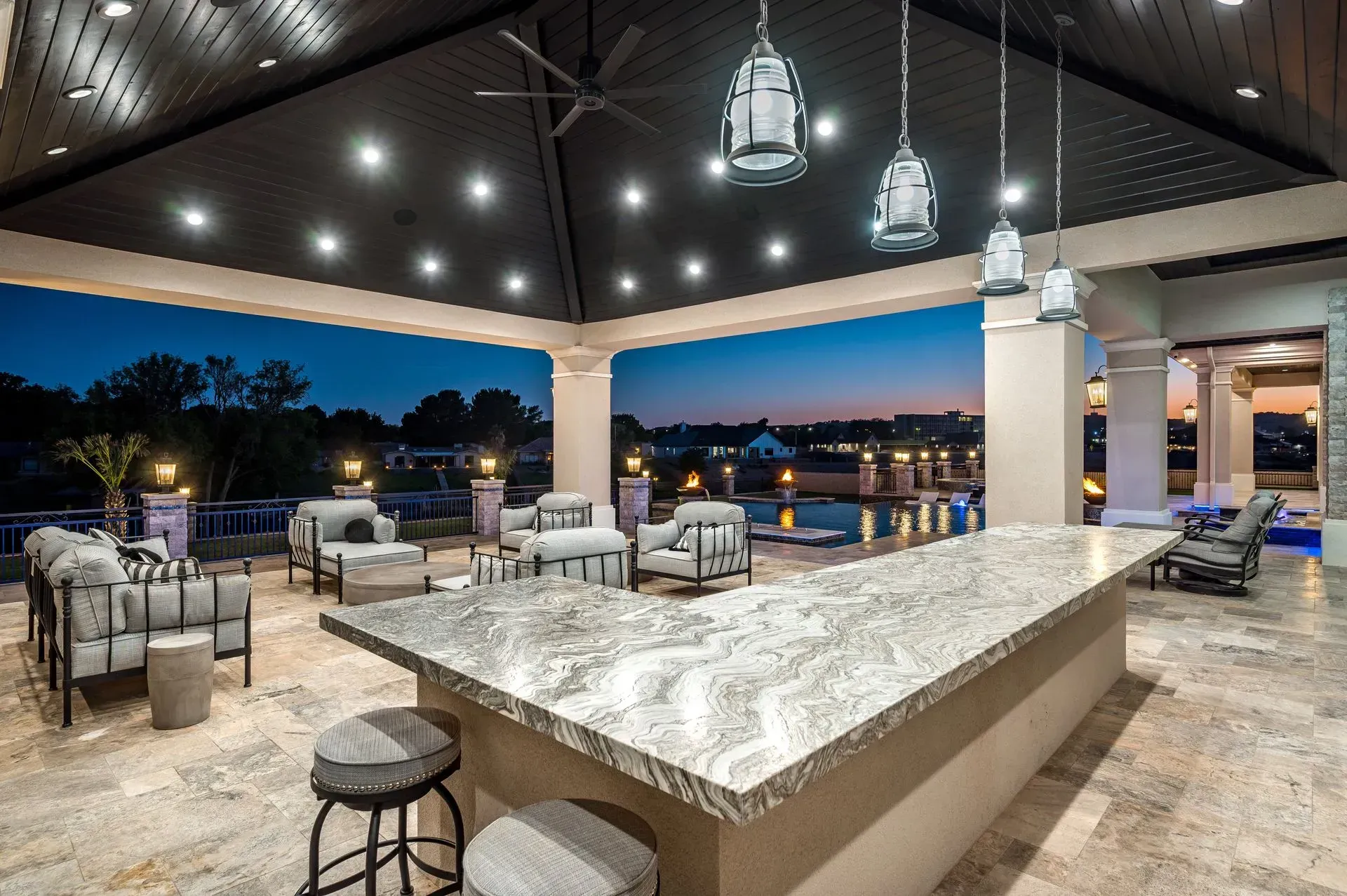 Outdoor patio with a bar, seating, and a view of the water at dusk.
