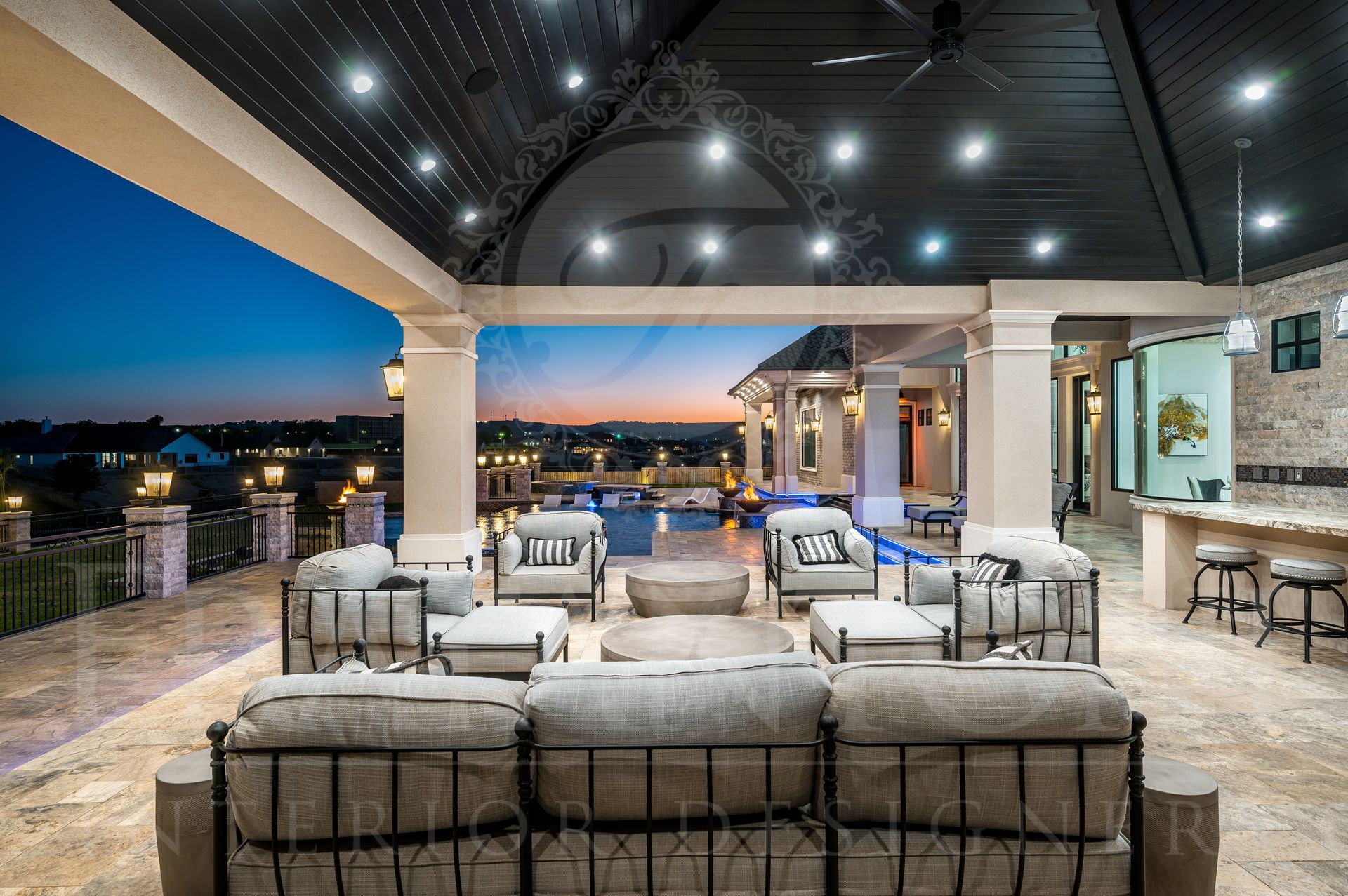 Outdoor patio with seating, lit at dusk, overlooking a pool and neighborhood.