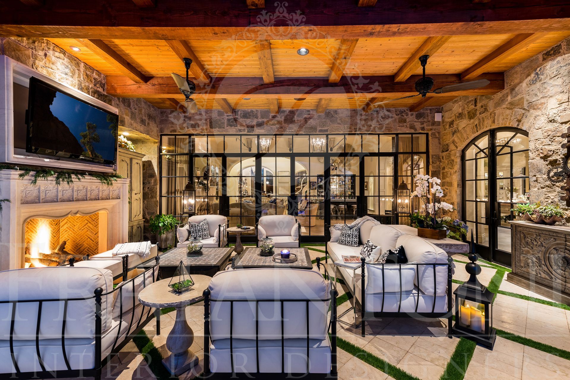 Luxurious outdoor living room with stone walls, fireplace, and black-framed glass doors designed by Fratantoni Interior Designers in scottsdale, arizona.
