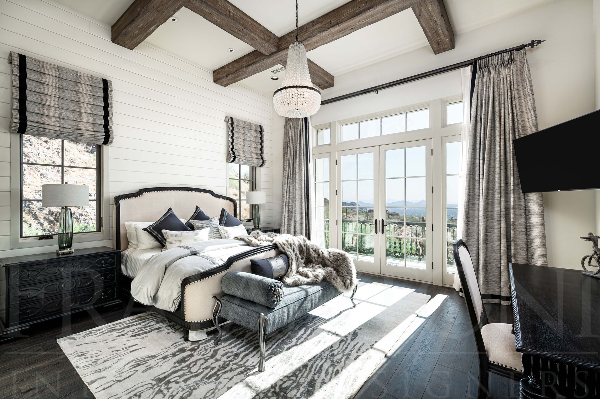Bright luxury bedroom with exposed beams, large windows, a balcony, French doors, king sized-bed, and desk overlooking desert and city views