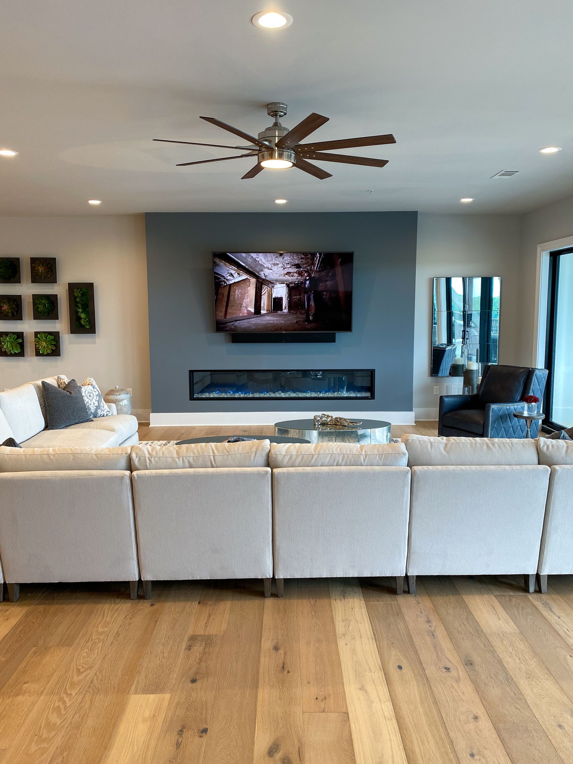 Modern living room with light sectional sofa, fireplace, large TV on blue wall, and hardwood floor.