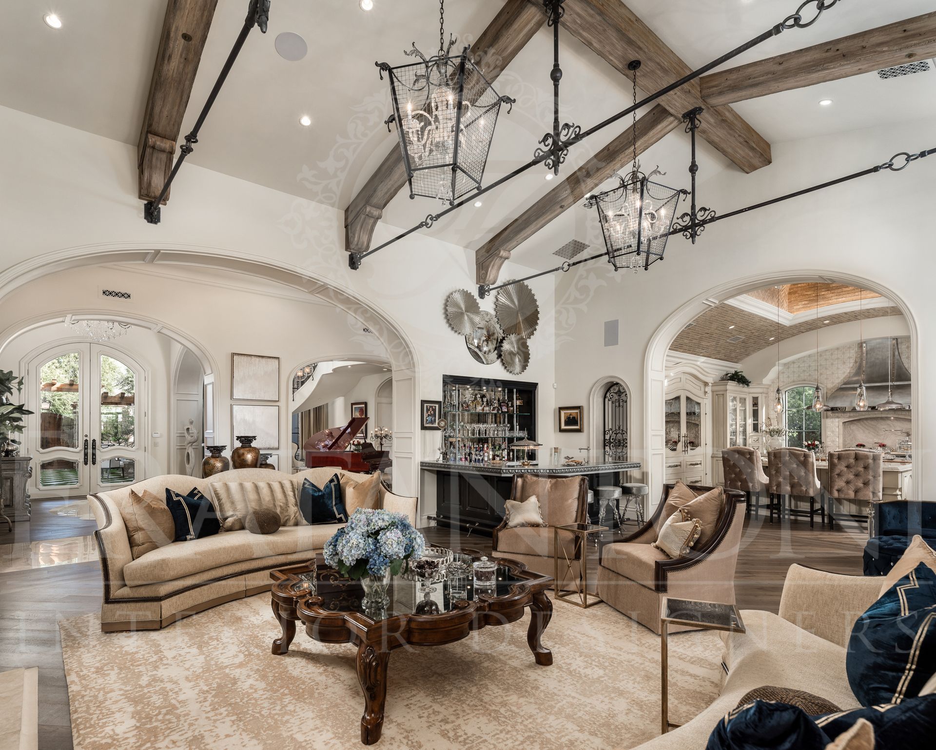 Luxurious living room with ornate furniture, high ceilings with wood beams, and arched doorways.