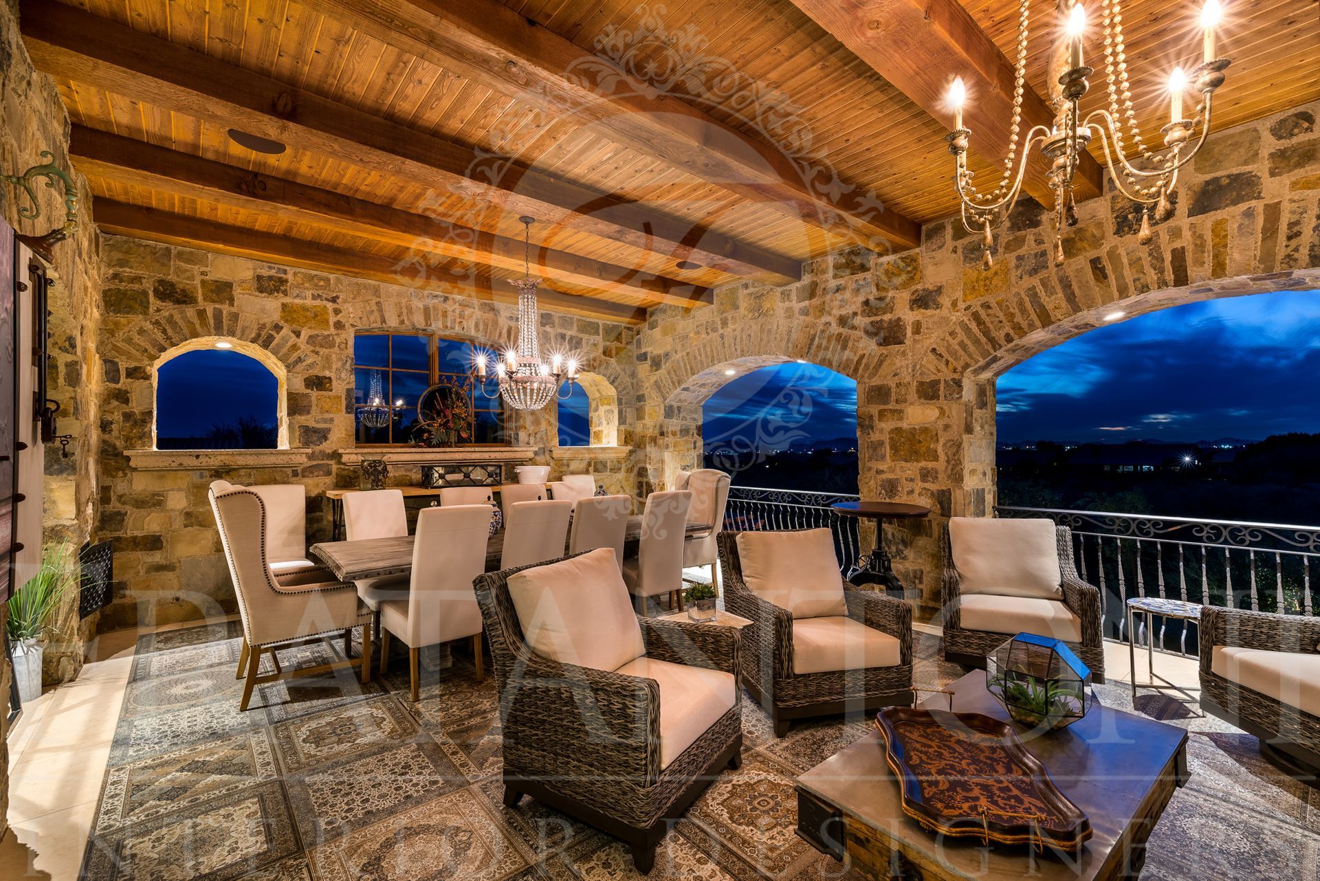 Stone-walled outdoor dining area with tables, chairs, and a chandelier, overlooking a desert at night view.