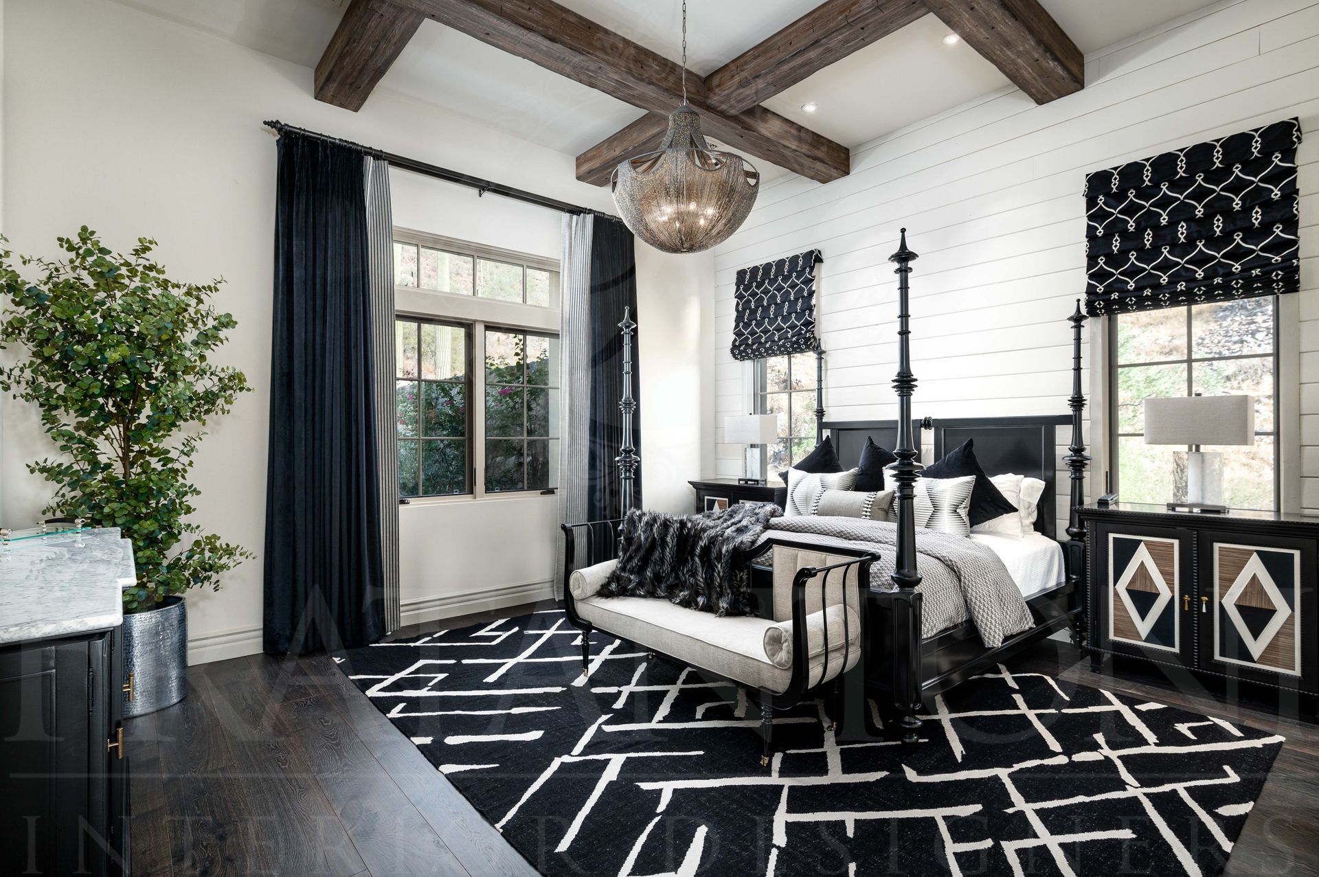 Black-and-white bedroom with canopy bed, patterned rug, dark curtains, and exposed wood beams.
