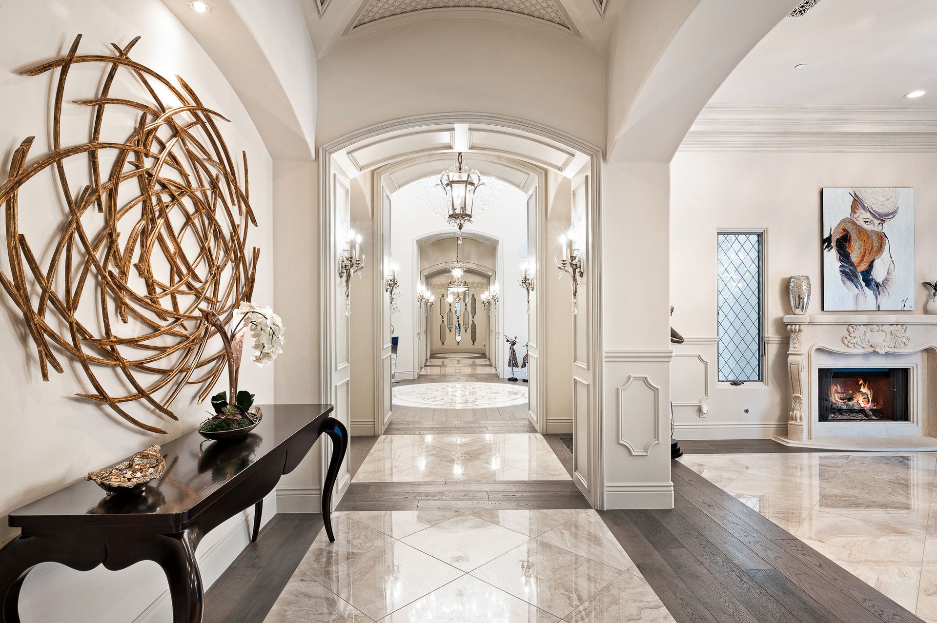 Elegant hallway with marble floors, artwork, fireplace, and chandelier lighting.