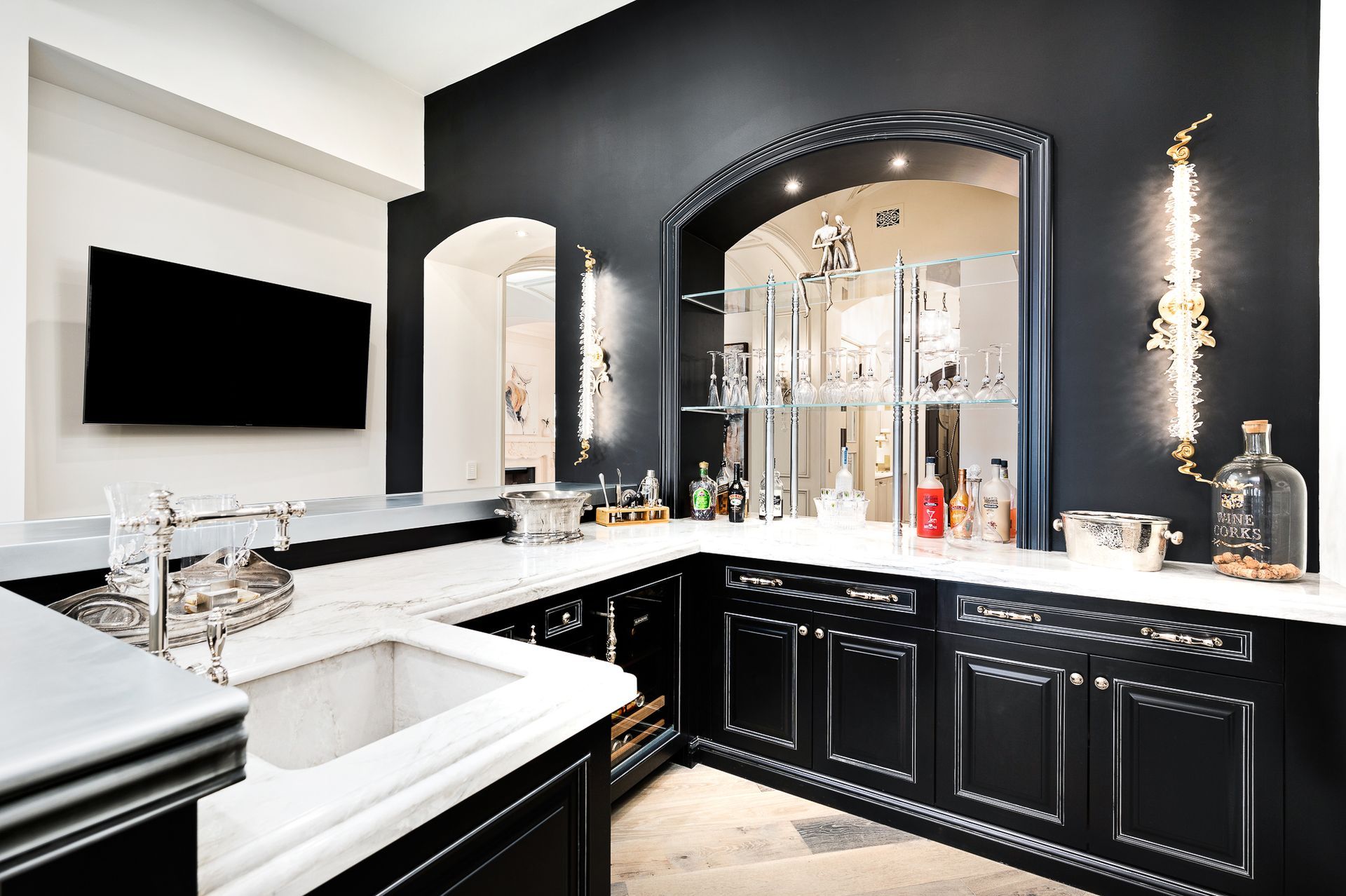 Black and white home bar with liquor bottles, sink, and a mounted TV.
