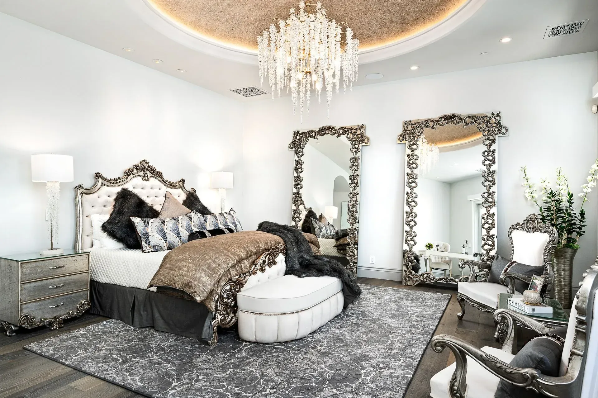 Luxurious bedroom with ornate furniture, two large mirrors, and a crystal chandelier.