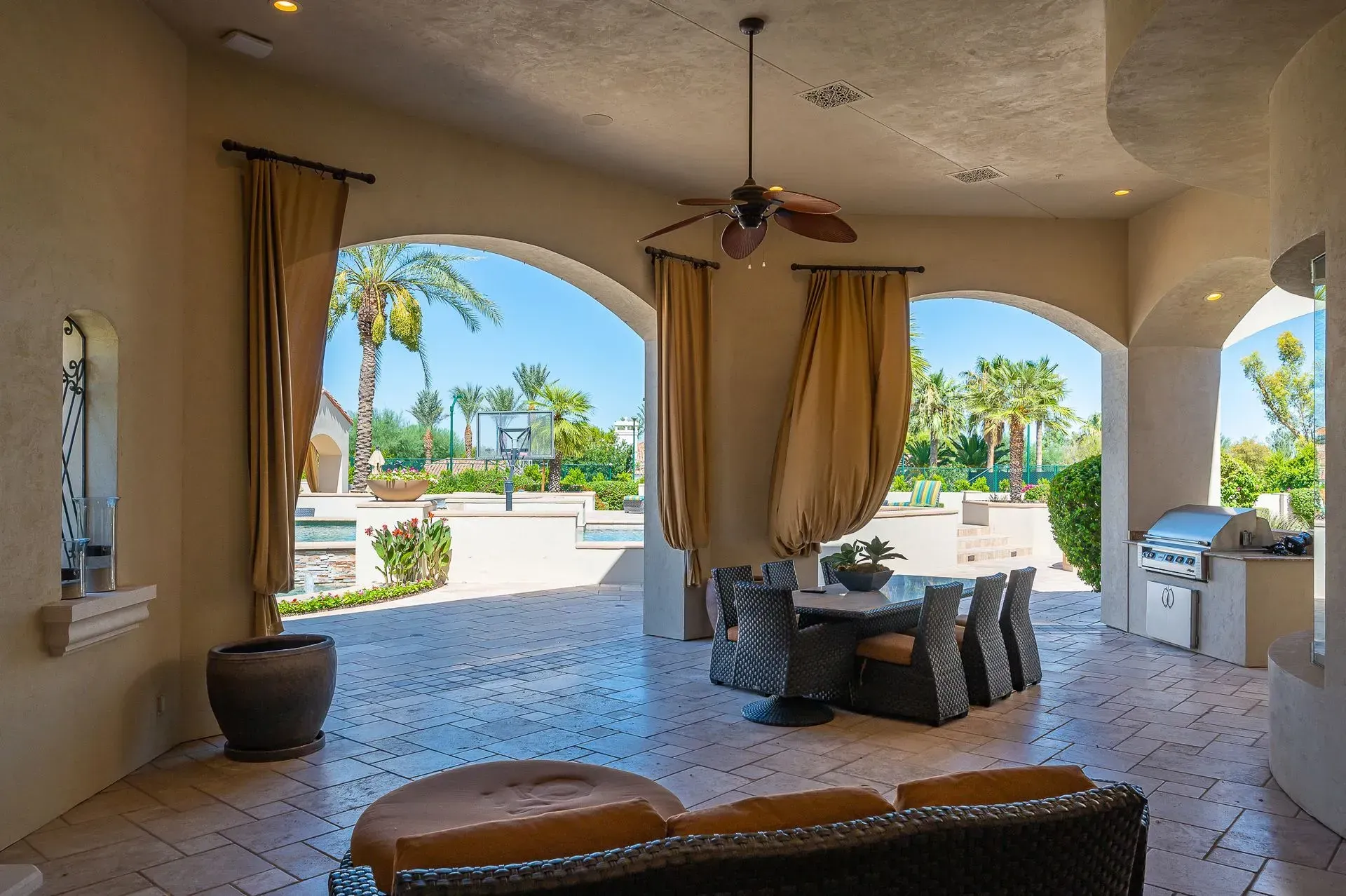 Outdoor patio with arched openings, table, and grill overlooking a pool.