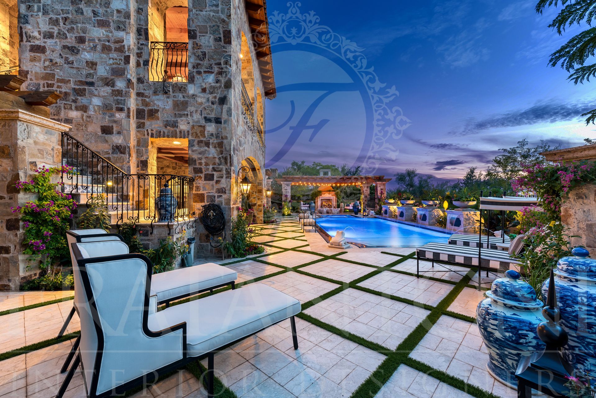 Stone villa with a resort-style pool and lounge chairs at dusk. Blue and white accents, exterior lighting, outdoor setting designed by Fratantoni Interior Designers.