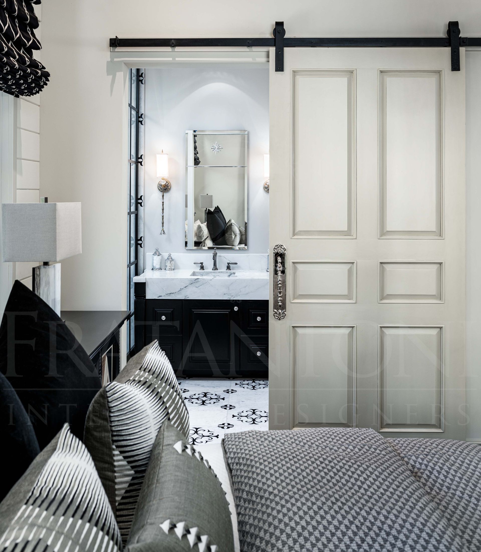 Bedroom with open sliding doors revealing a bright bathroom vanity mirror, and mosaic tile floors.