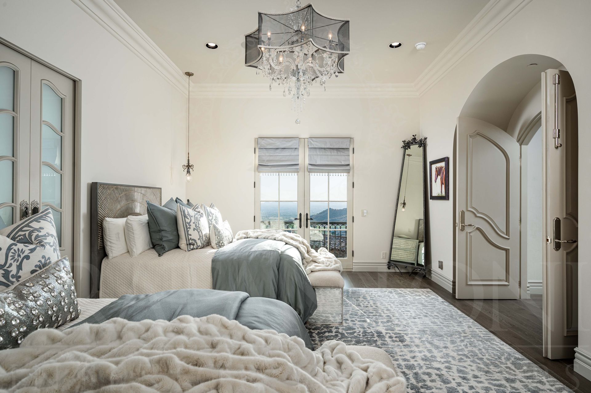 Bright elegant bedroom with two tufted beds, chandelier, standing mirror, and balcony doors overlooking the desert mountains in arizona.