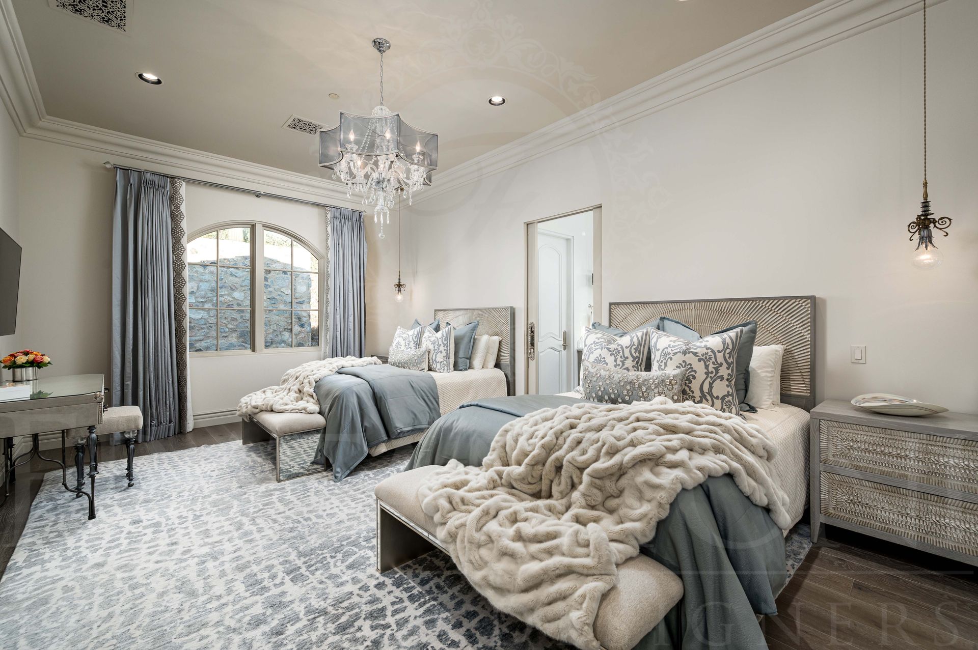 Elegant gray-and-white guest bedroom with two beds, chandelier, large window, custom drapery, and plush rug