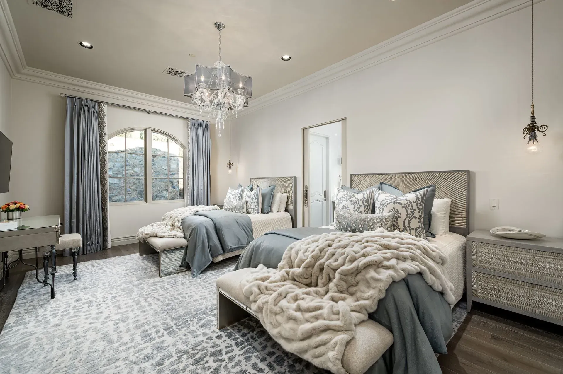 Bedroom with two beds, gray and white decor, rug, window, chandelier, and a mirrored nightstand.