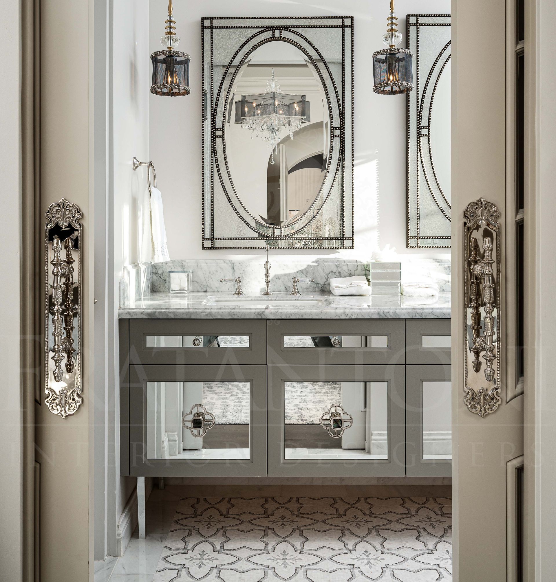 Elegant mirrored bathroom vanity with large mirrors, hanging lights, marble countertops, and patterned floor tiles behind ornate pocket doors designed by fratantoni interior designers in scottsdale, arizona
