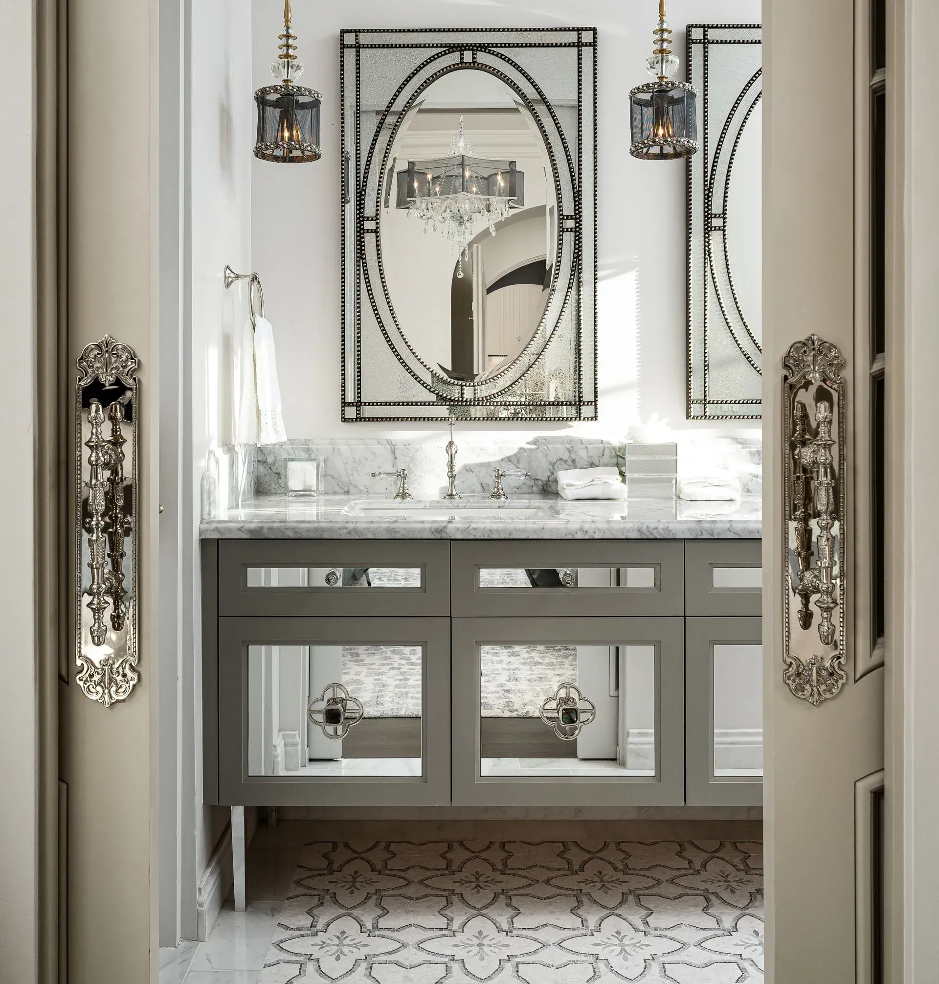 Bathroom interior with a gray vanity, mirrored accents, and decorative light fixtures.