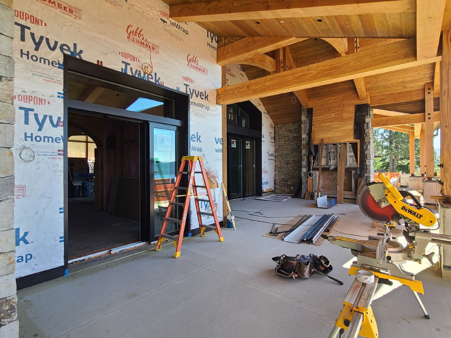 Construction site of a building with stone and wood elements. A ladder, saw, and windows are visible.
