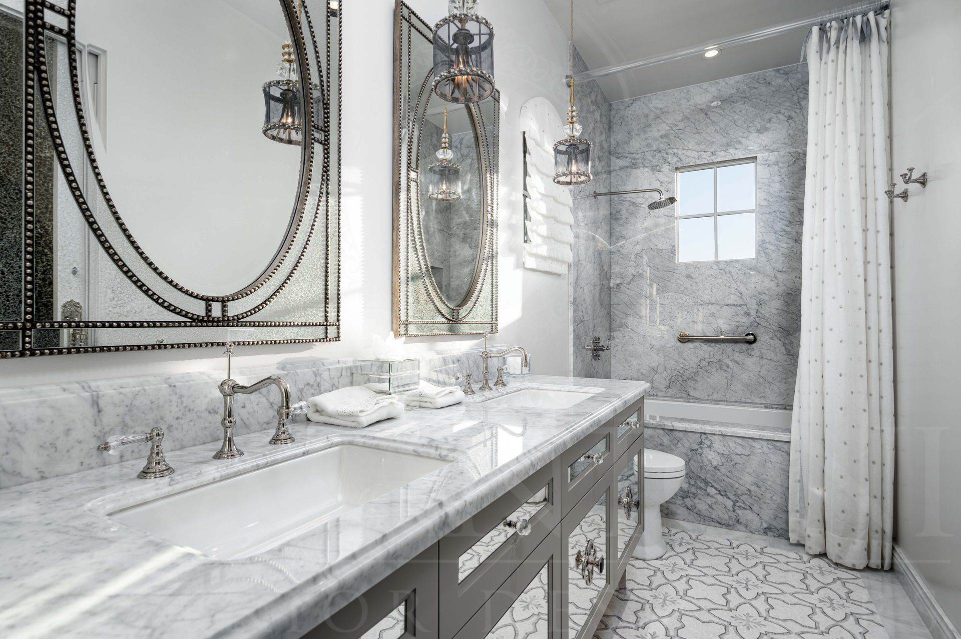 Elegant bathroom vanity with double mirrors, gray cabinets with mirror inlays, white marble countertop, a marble shower and bathtub, and patterned mosaic floor tiles