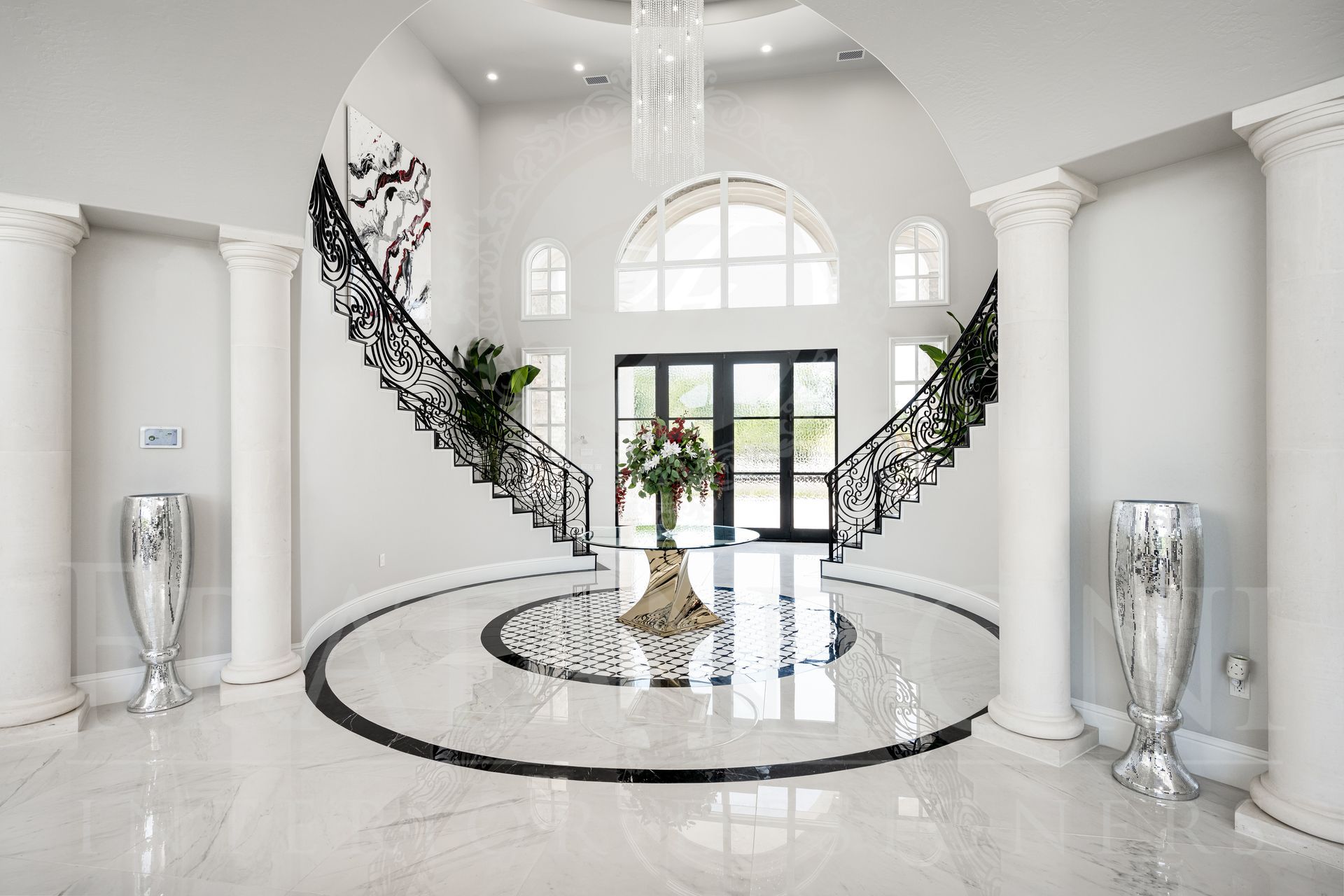Grand white foyer with curved staircase, marble floors, black railings, and decorative vases.