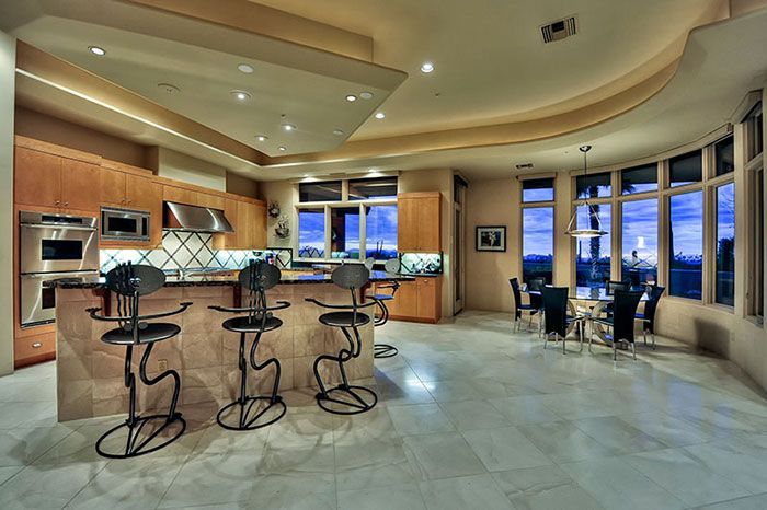 A kitchen with a large island and stools and a dining room with a table and chairs.