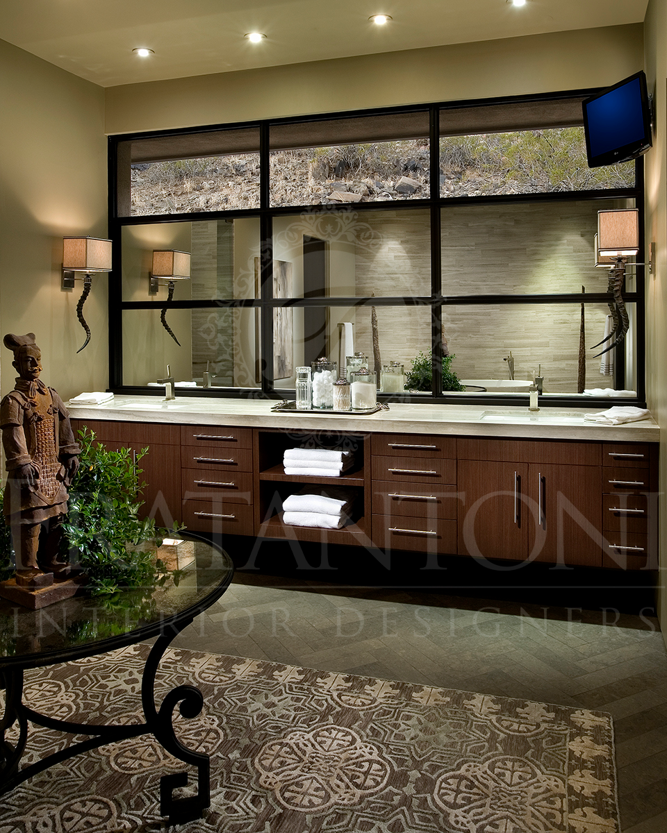 A luxurious bathroom vanity with wooden cabinets, dual sinks, a large black-framed mirror, and a decorative statue.