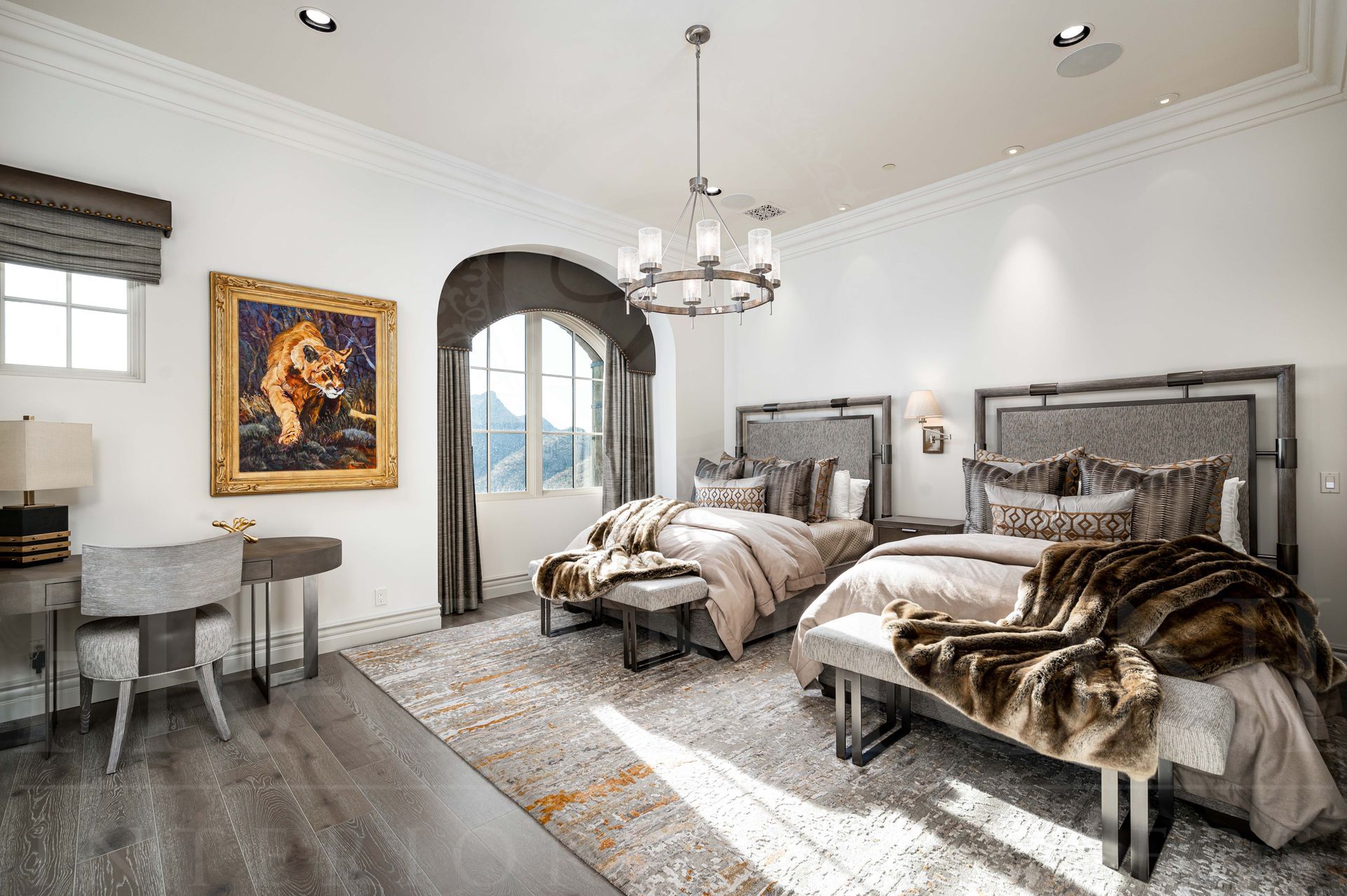 Bright bedroom with two queen beds, hanging chandelier, arched window with custom drapery, and desk by the wall designed by luxury interior designers in arizona