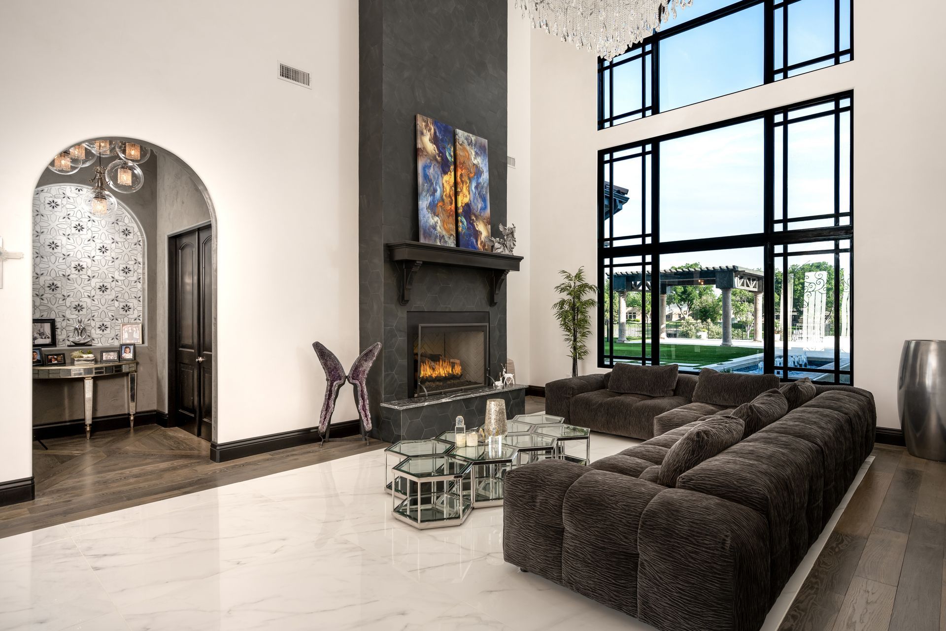 A modern living room with a fireplace, large windows, and gray sectional sofa.